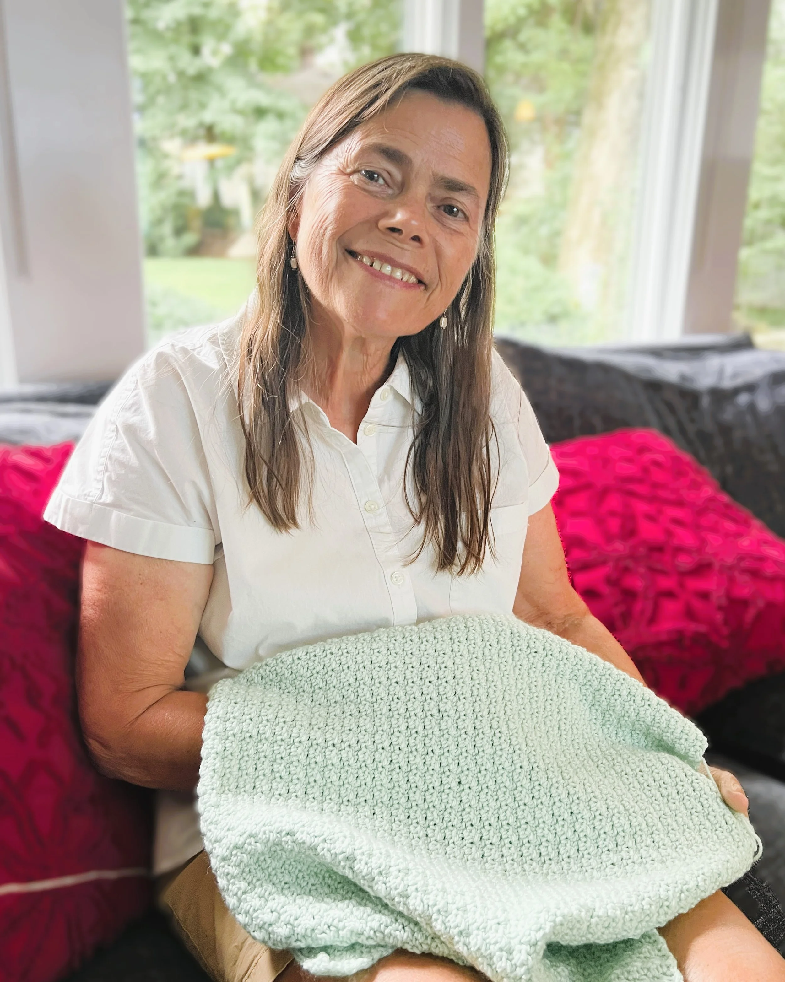 instructor of crochet sitting in her livingroom with a crocheted baby afghan