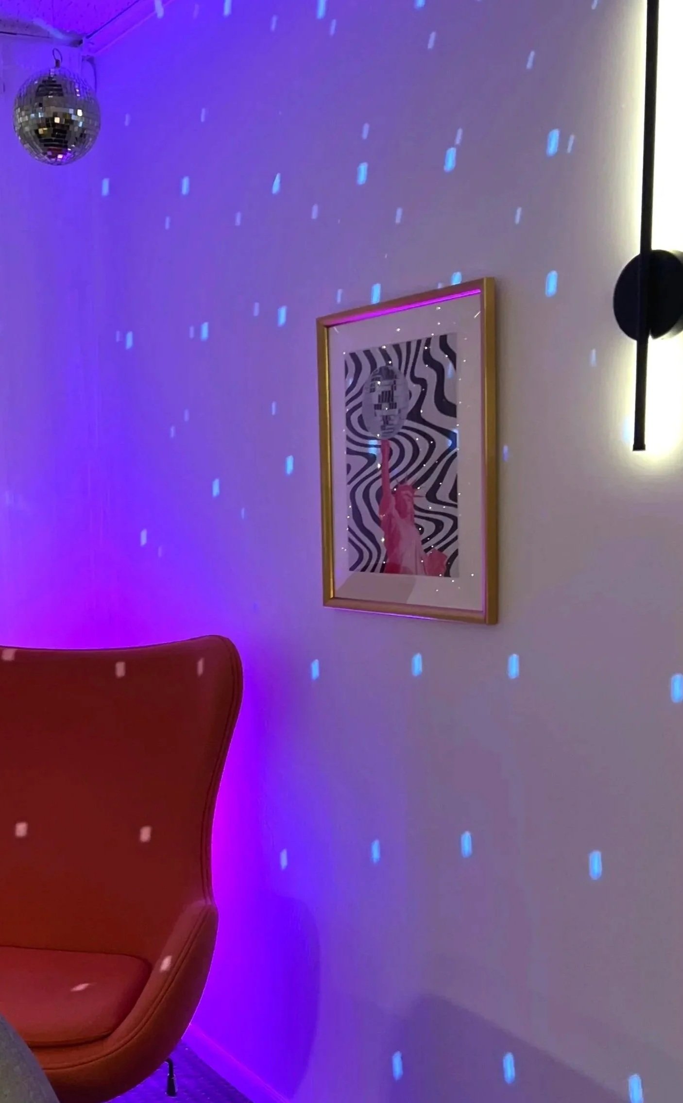 A red chair, wall art, disco ball, and glowing blue-pink lights set the scene for a colorful, modern party room vibe