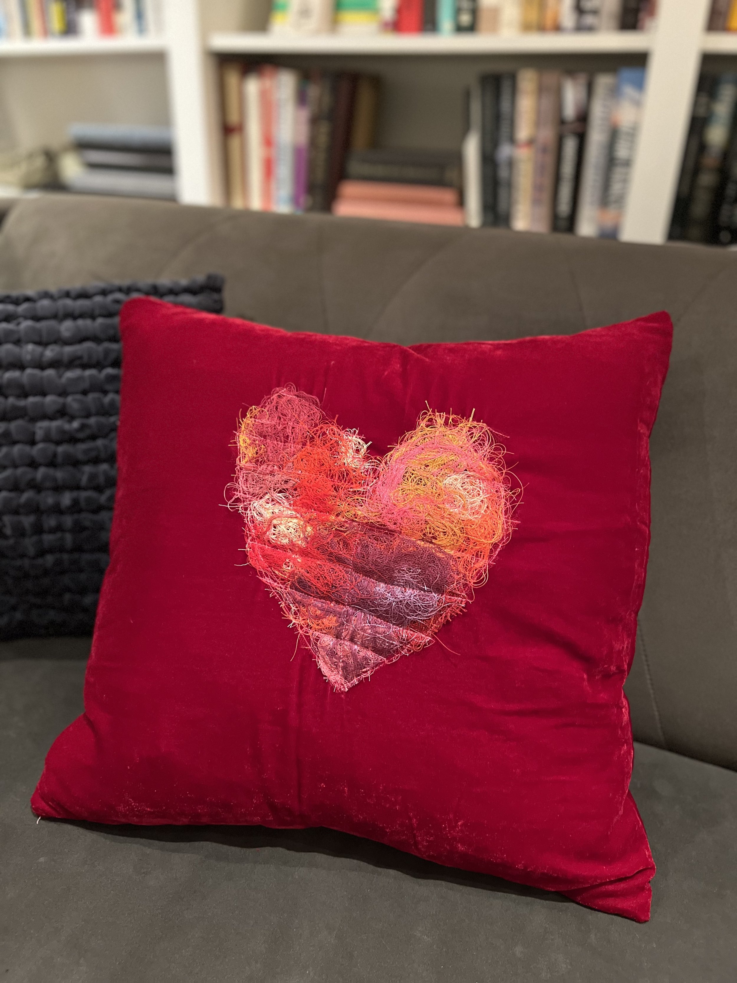 red velvet pillow with multi colored pink orange heart made out of sewn on threads