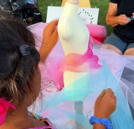 back of little girl draping a mini mannequin with pink and turquoise tulle