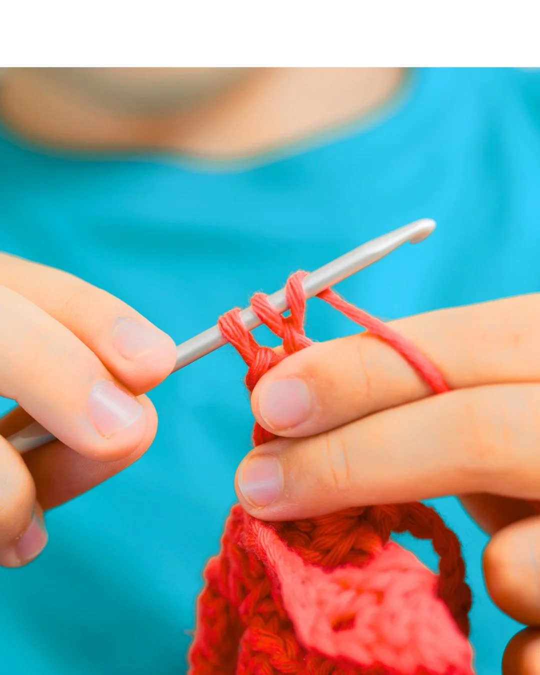 closeup of child in blue t-shirt crocheting with red yarn