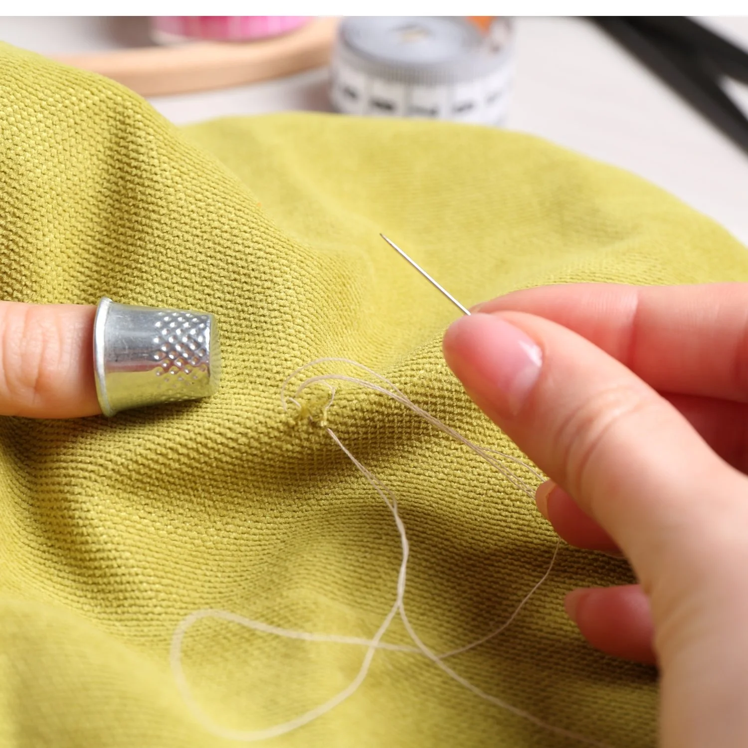 woman's hands mending a yellow sweater by hand sewing with needle, thread and thimble