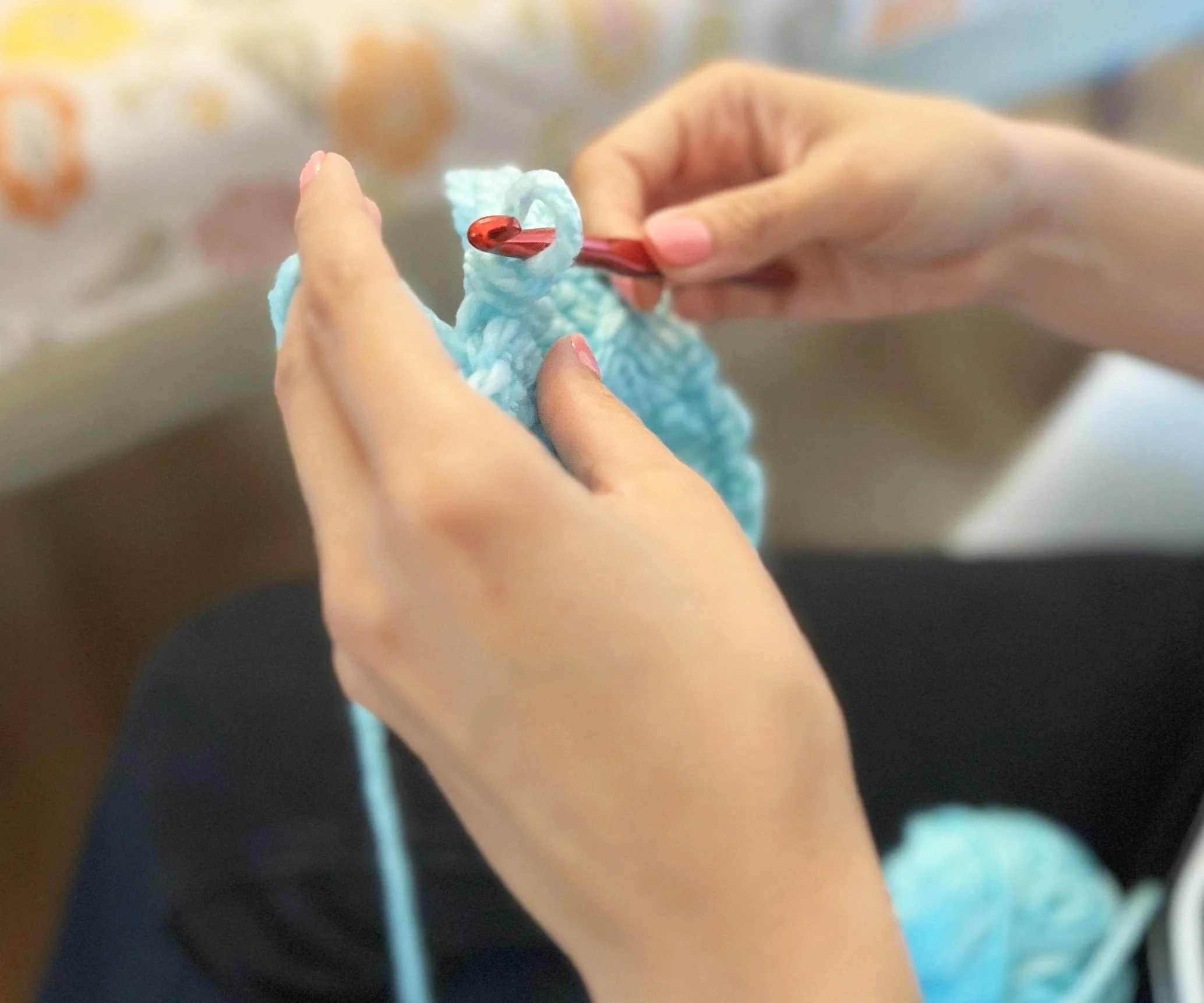 lady with pink finger nails crocheting with blue yarn