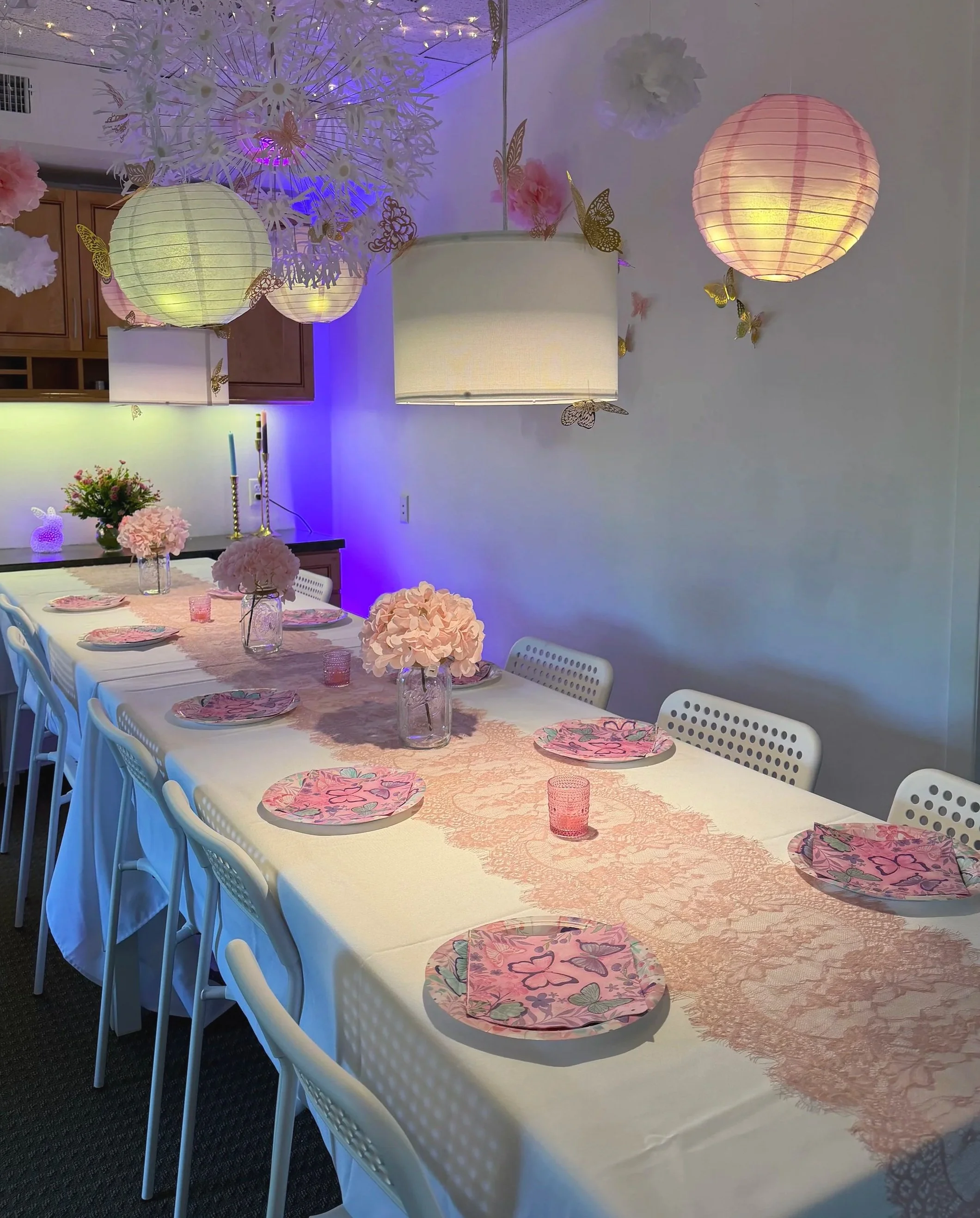 Long white table with pink lace runner and plates, pink flowers, lanterns, and butterflies