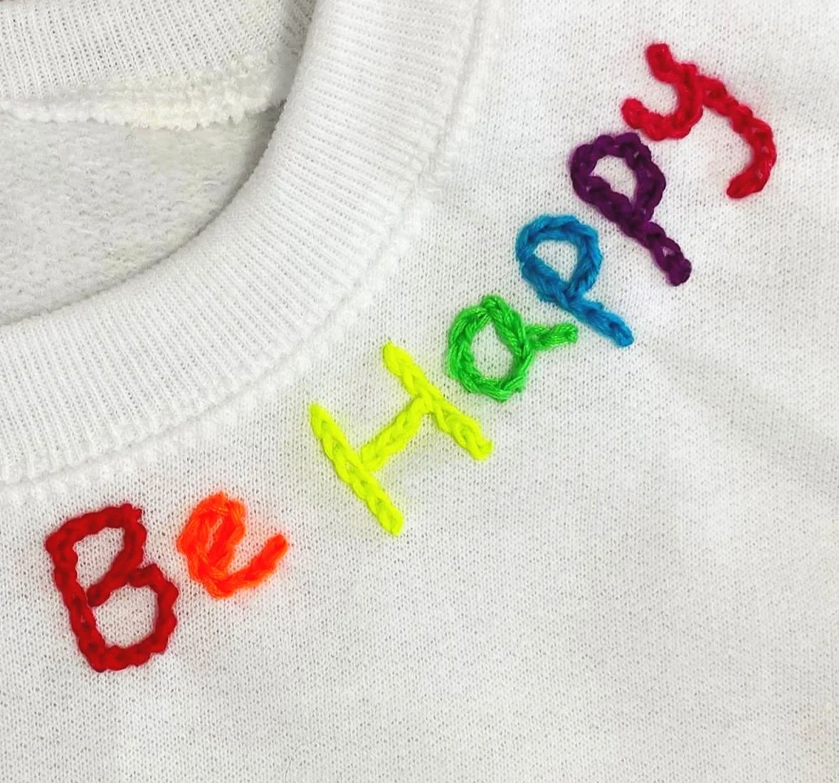 neon color embroidery words be happy on a white sweatshirt