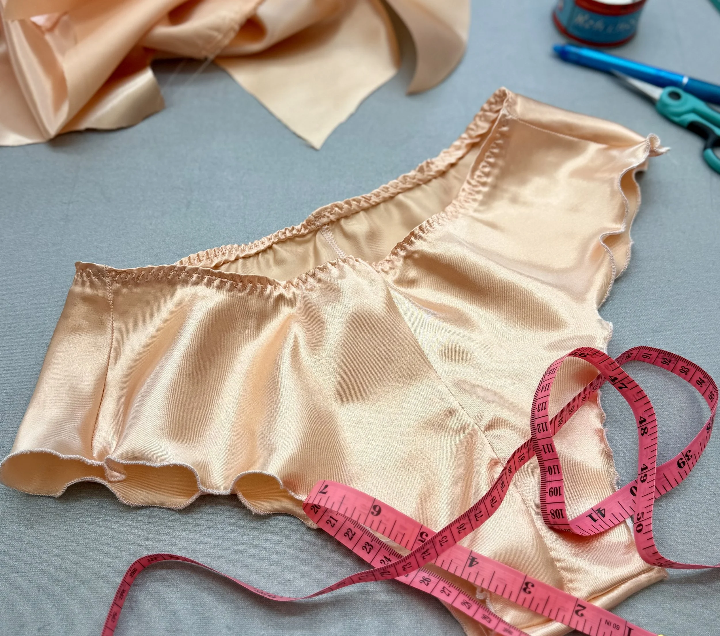 peach colored silk satin French knickers with a measuring tape over them