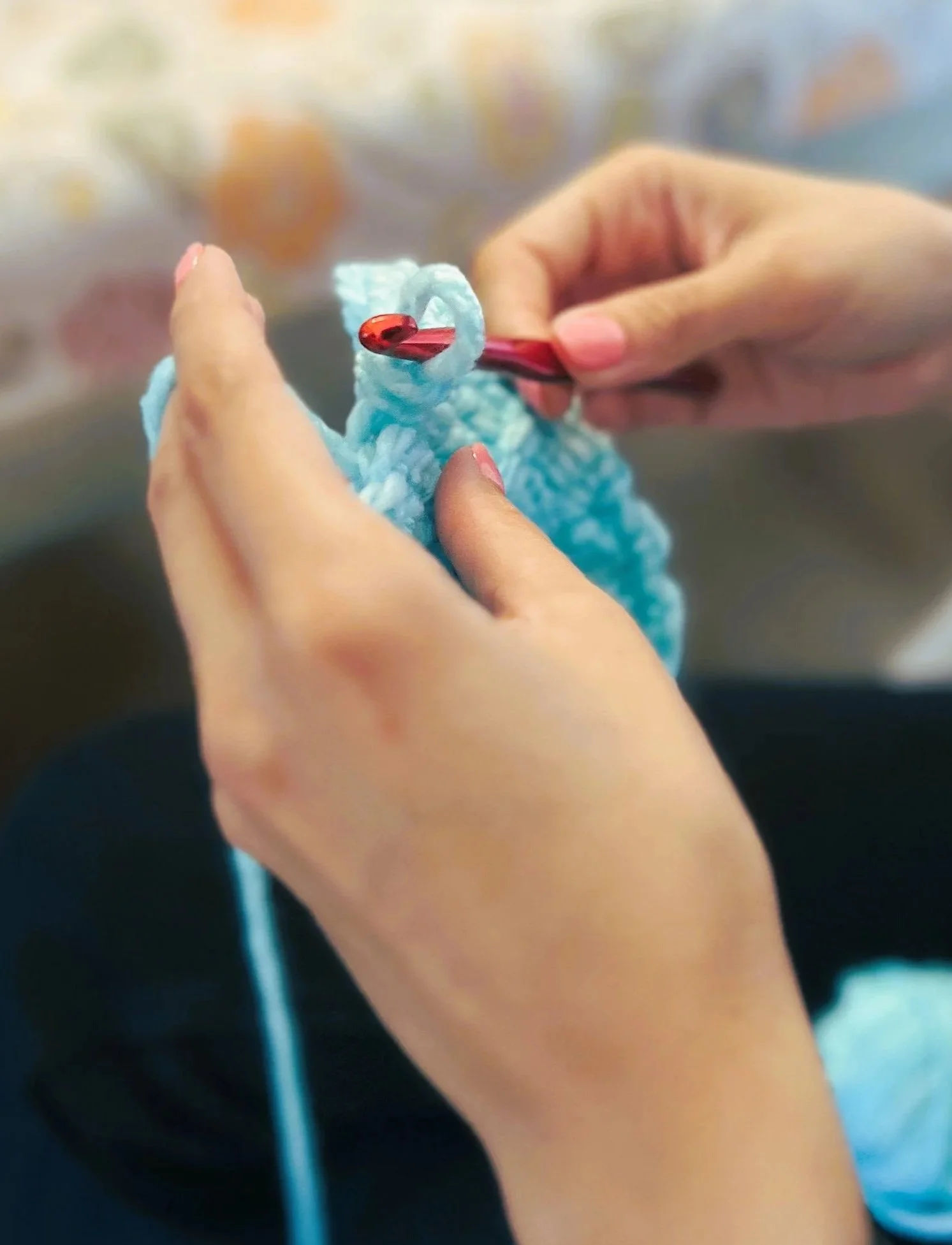 women's hands crocheting with red hook and blue yarn