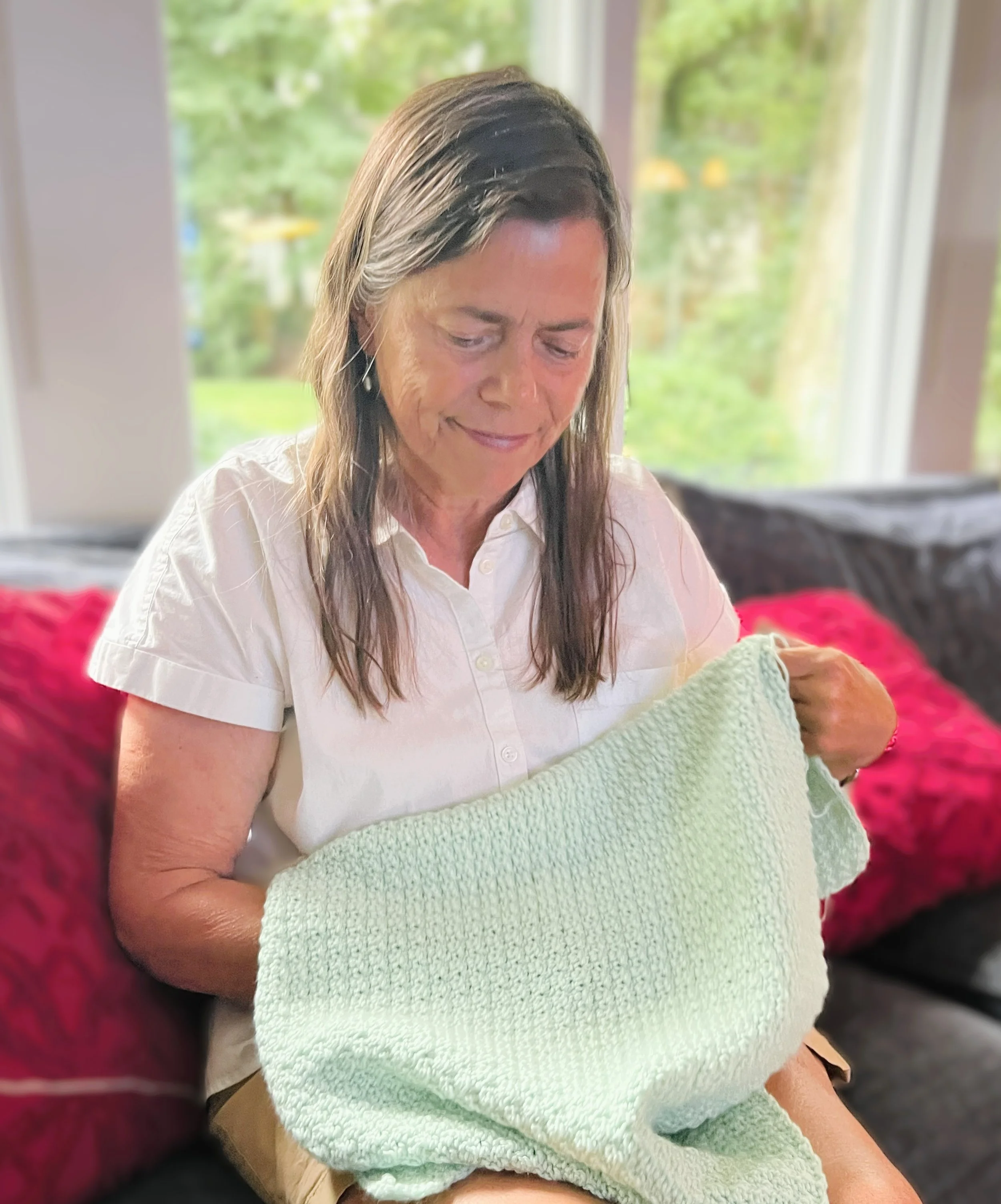crochet instructor sitting in her livingroom with a pastel colored crocheted afghan