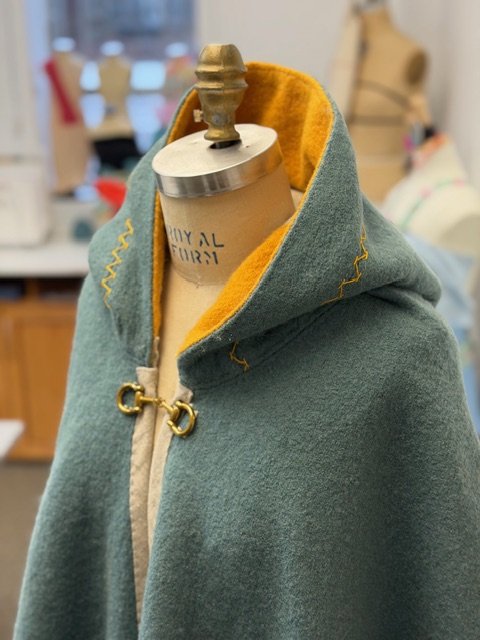 green wool hooded cape with yellow stitching on a mannequin