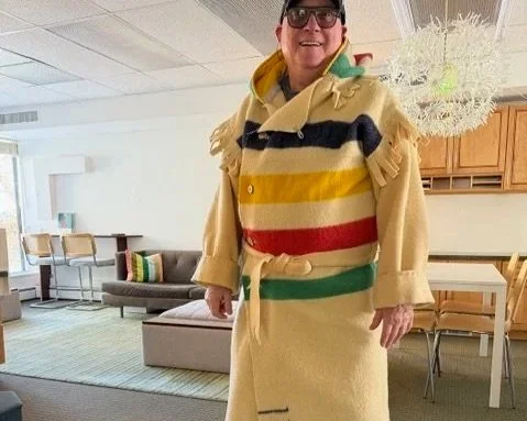 man in sunglasses standing in livingroom in a hudson bay blanket coat