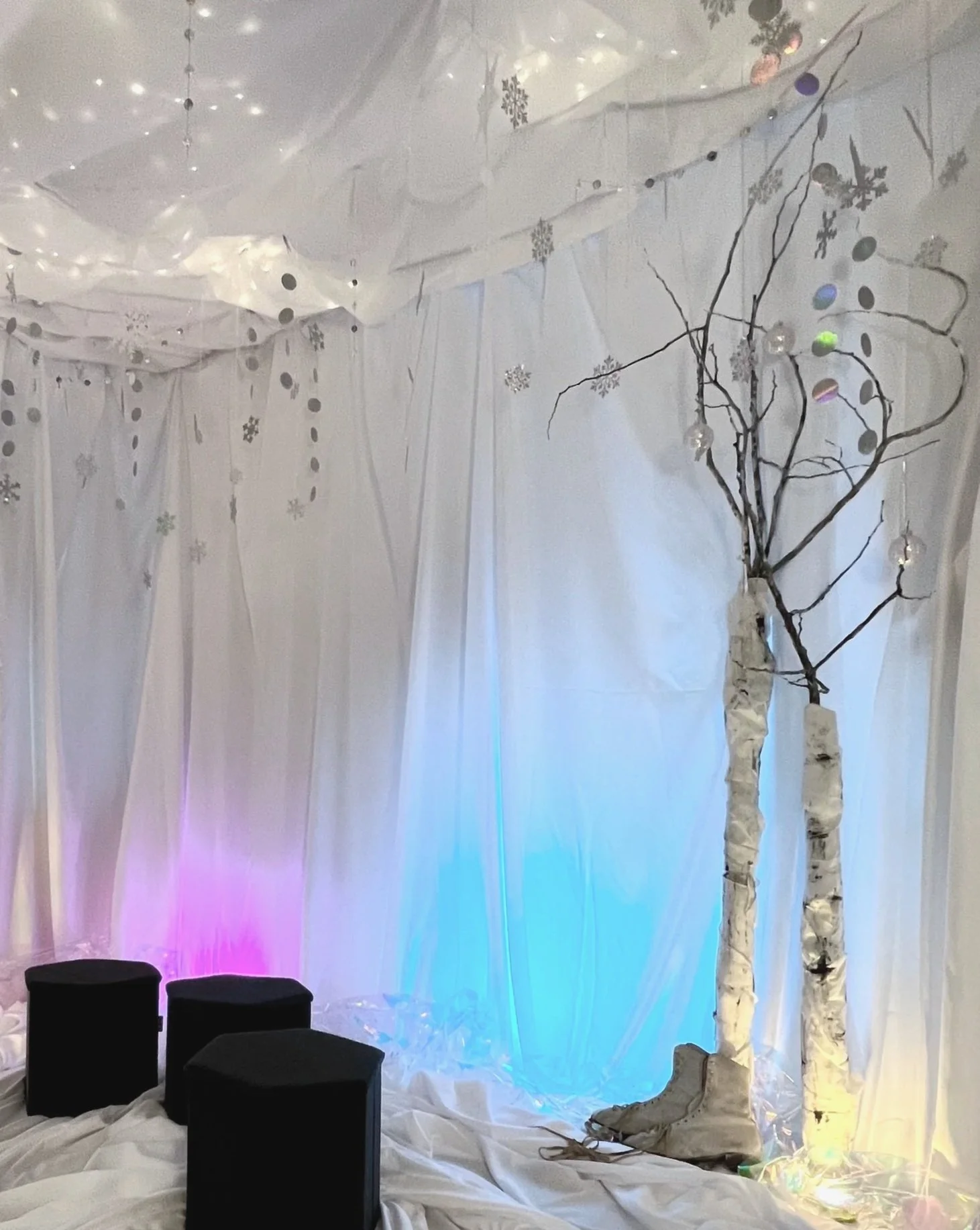 Black stools and fabric covered white walls with fairy lights and birch trees inside a room