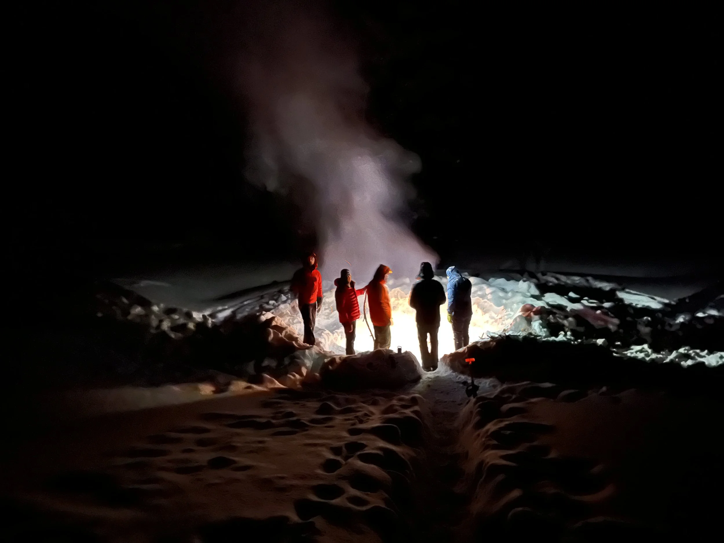 Backcountry skiers gathered around a bonfire in Montana with Bozeman ski touring guides