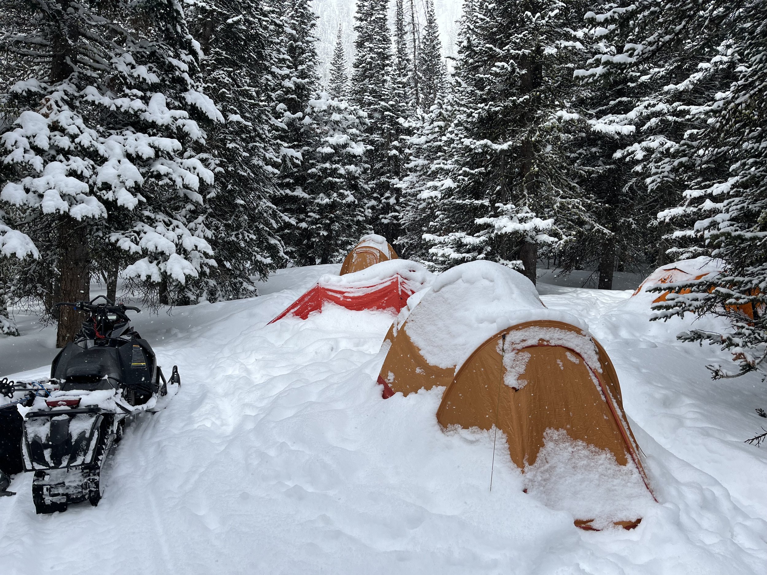 Snow covered tents at ski basecamp in Montana with snowmobile and ski touring guides