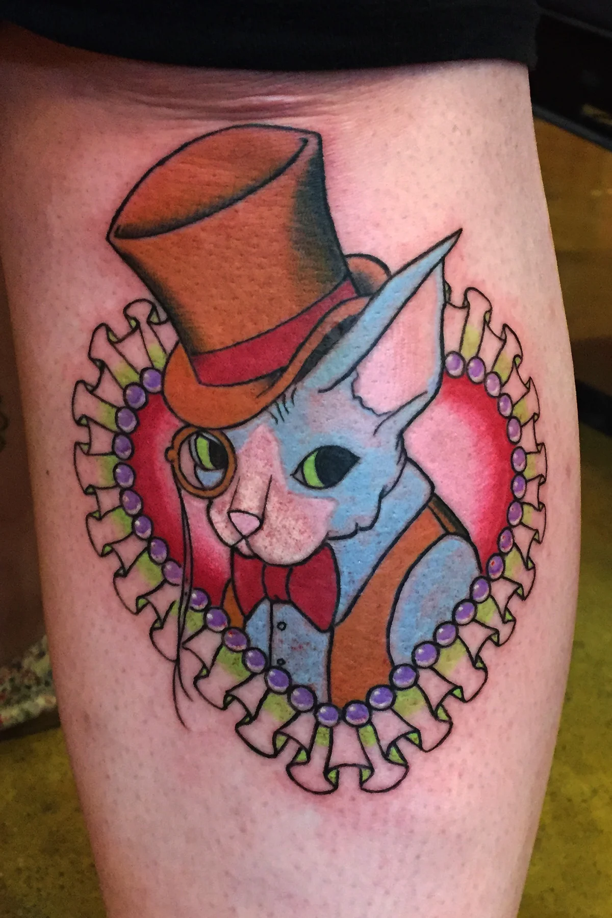 Gentleman Sphinx cat in a top hat, vest and monocle with in fancy heart, color tattoo on shin half leg sleeve. 