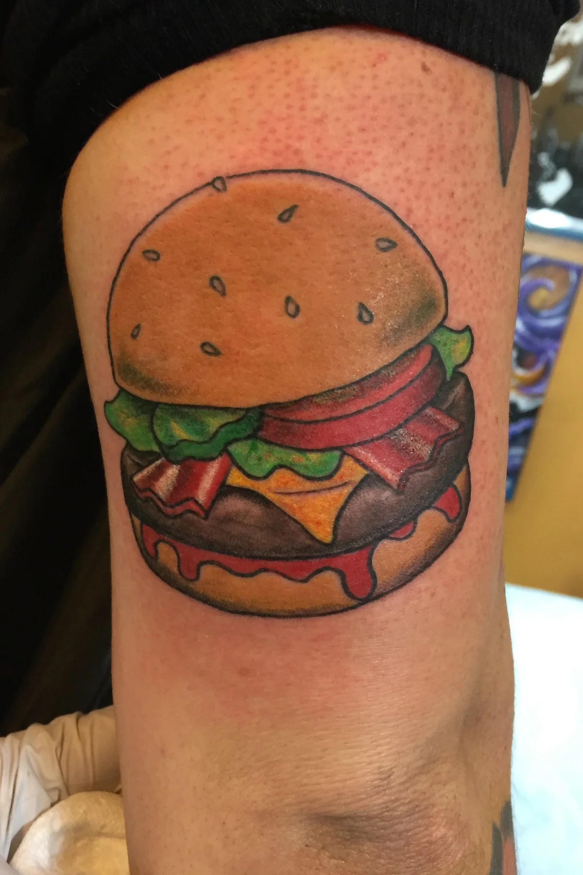 Bacon cheese burger on a sesame bun. Half arm sleeve color tattoo. 