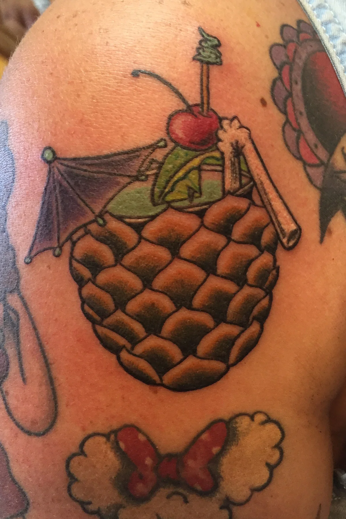 Pineapple cocktail with an umbrella and straw upper shoulder full sleeve color tattoo. 
