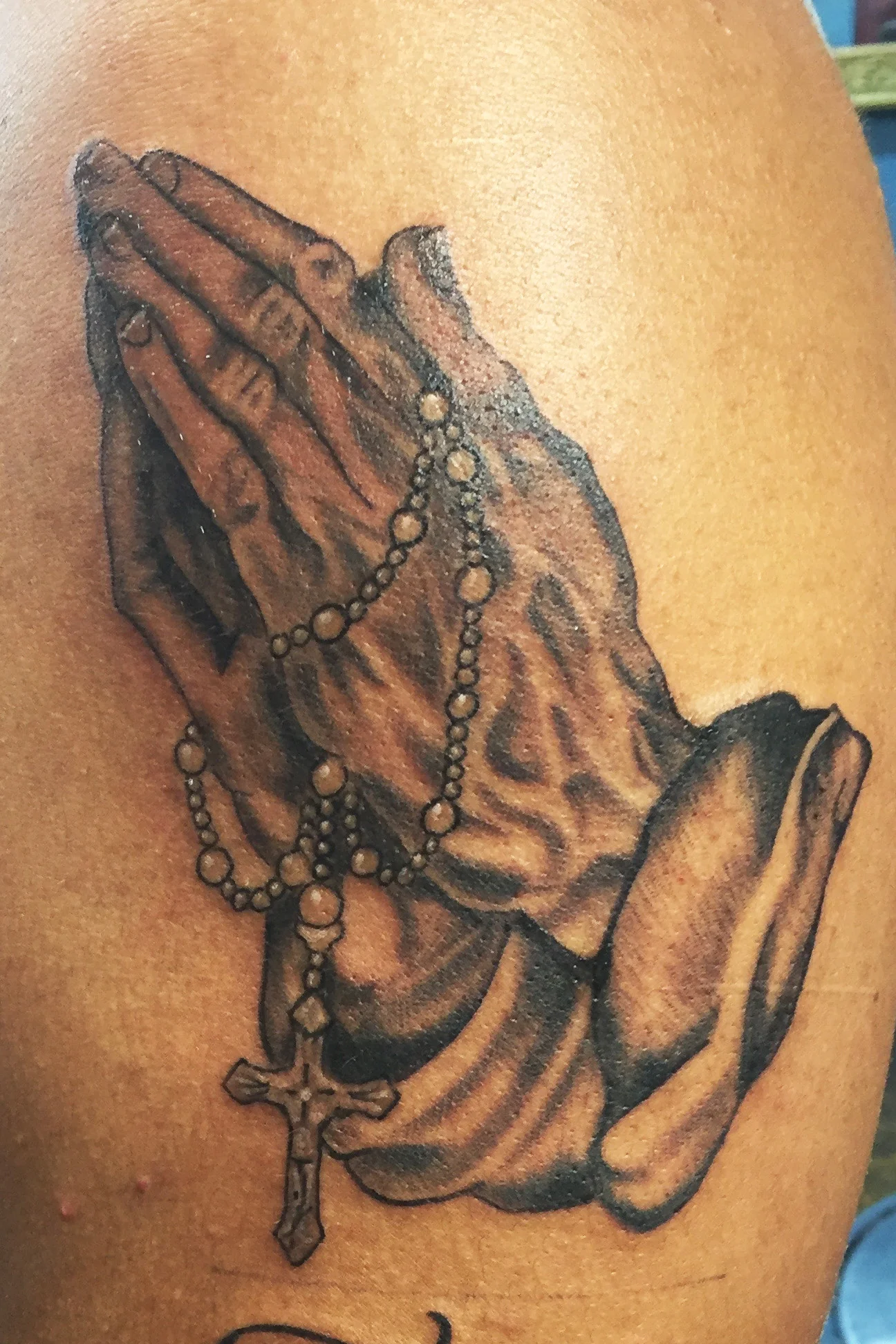 Praying hands with rosary beads and cross. Black and gray tattoo on upper arm, half sleeve