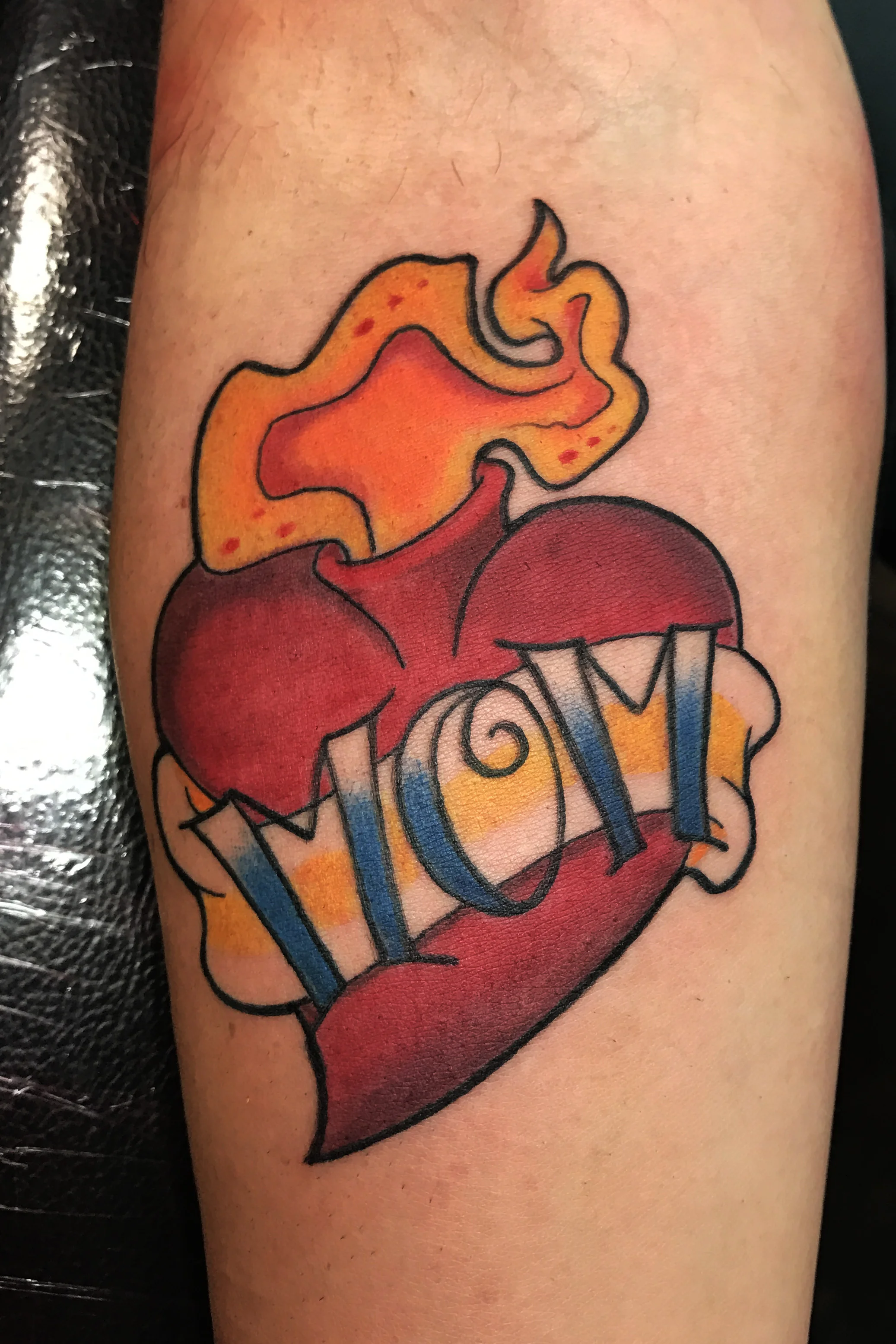 Heart for Mom. Sacred flaming heart. Mom lettering in a banner. Leg tattoo, traditional color.