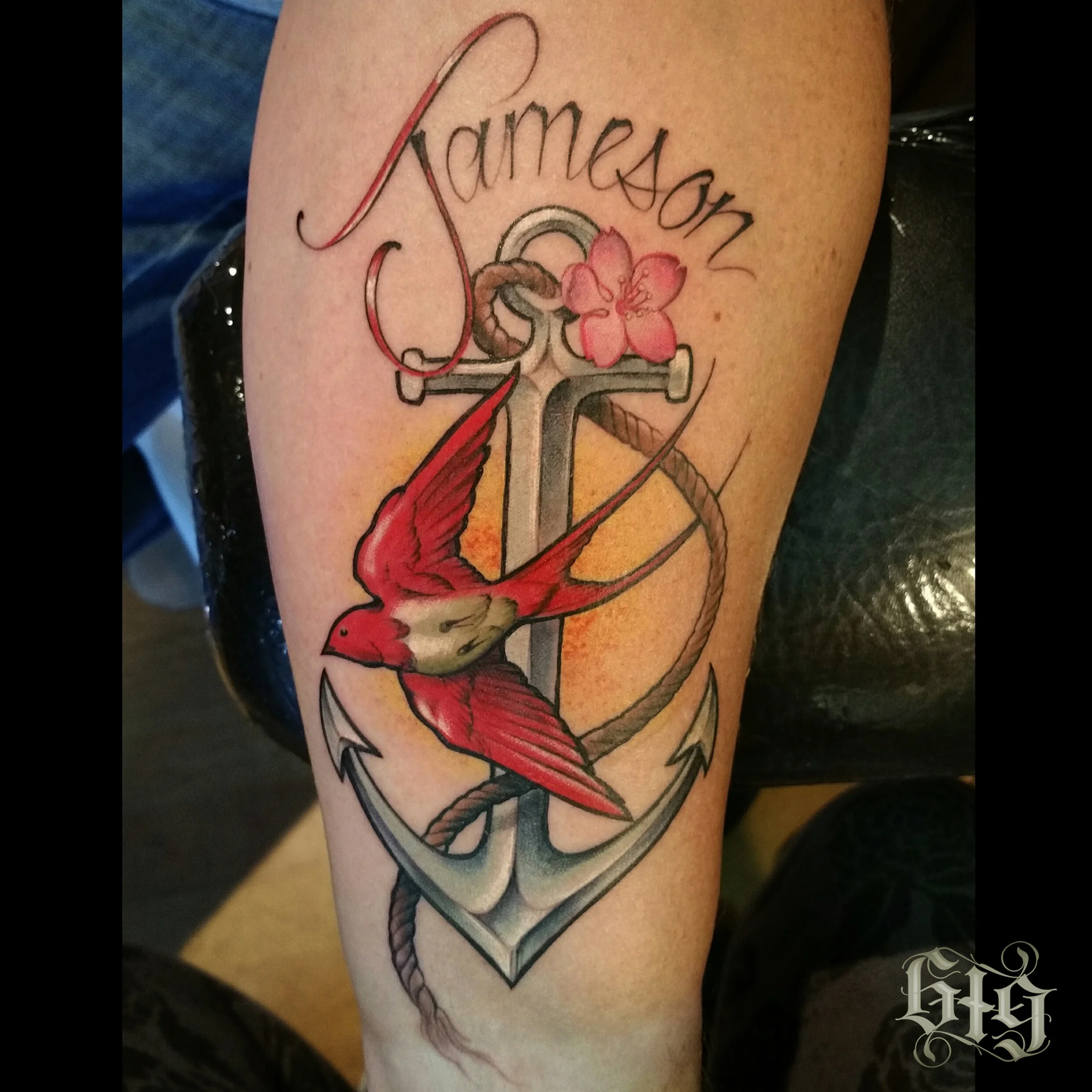 Red sparrow flying over an anchor with a pink flower and rope. "Jameson" cursive lettering. In color half leg sleeve tattoo.