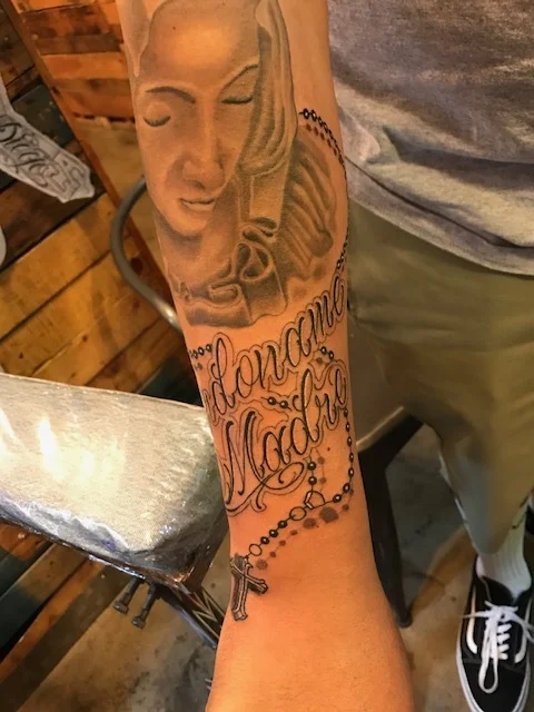Fine detail lettering and rosary black and gray forarm tattoo