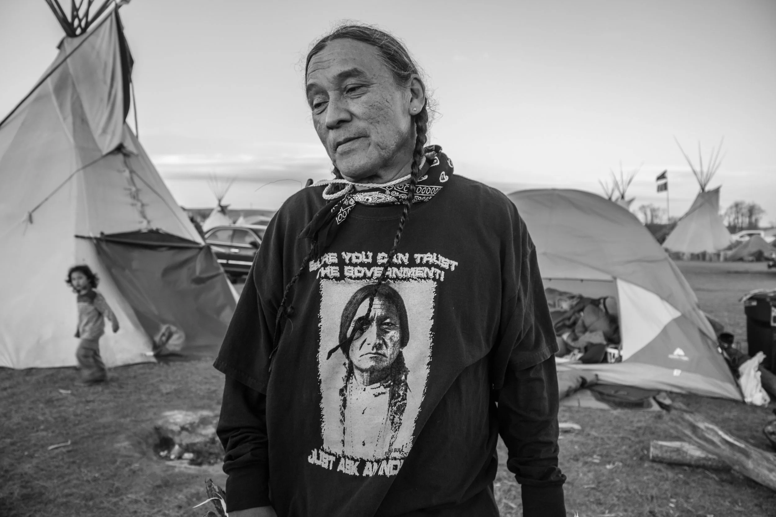 A man entrusted with the security of the Oceti Sakowin main camp wears a shirt with a portrait of Sitting Bull, which reads "Sure you can trust the government! Just ask an Indian!" "What white man can say I ever stole his land or a penny of his mon