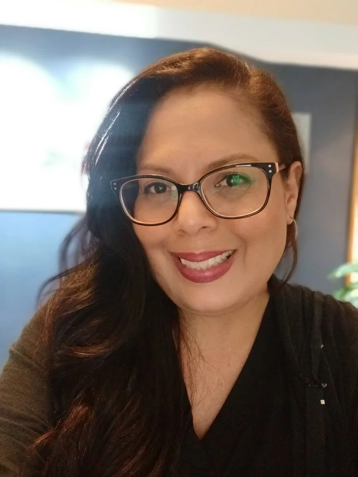Scenic view of a turquoise lake with purple flowers in foreground, snow-capped mountains in the background, and a clear blue sky.