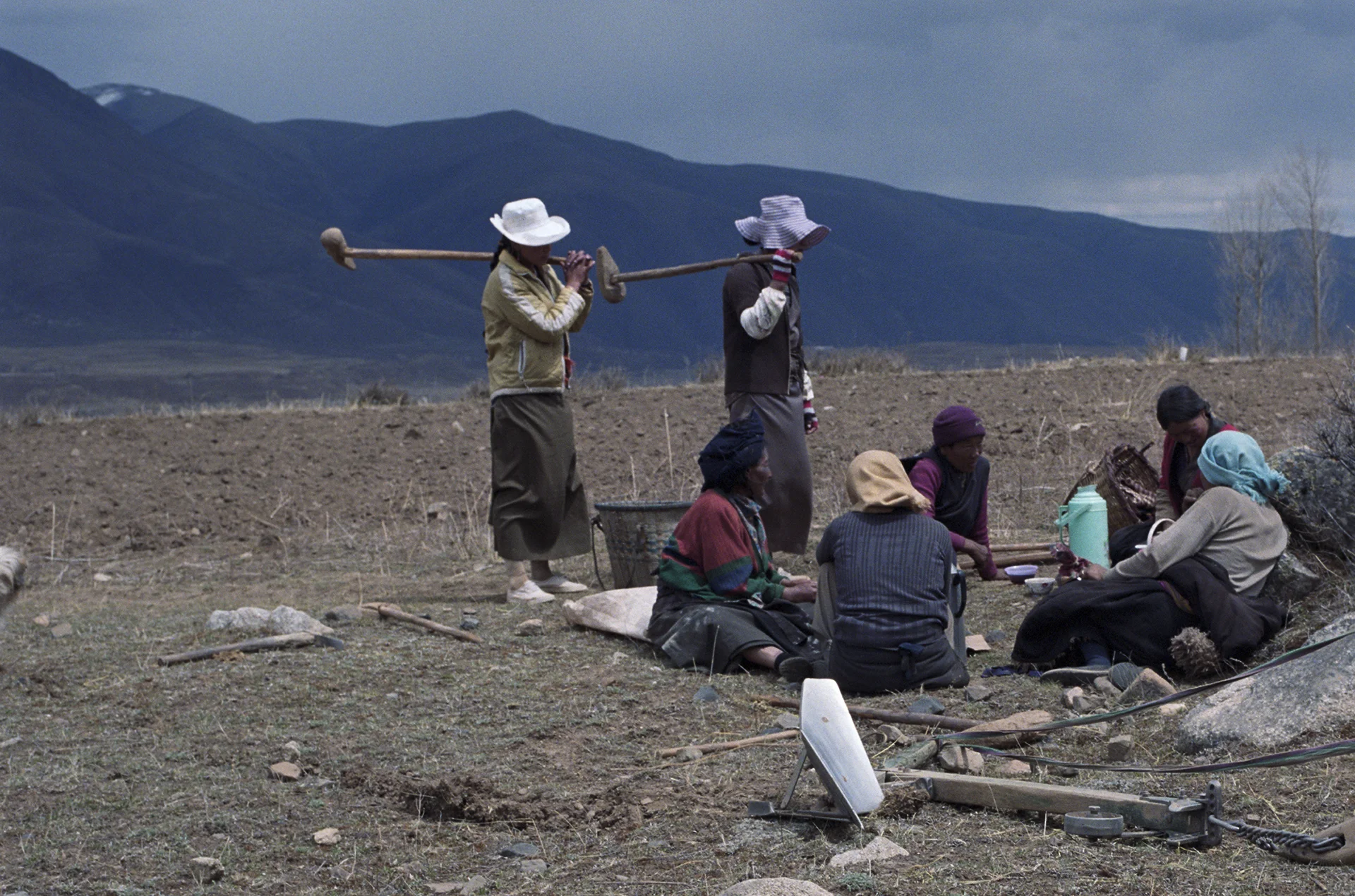 2010, near Kandze - men join the women for lunch. The equipment over their shoulder is used to break up lumps of hard soil. But there is a metal plow in the forefront. A yak will be used to pull it through the earth.