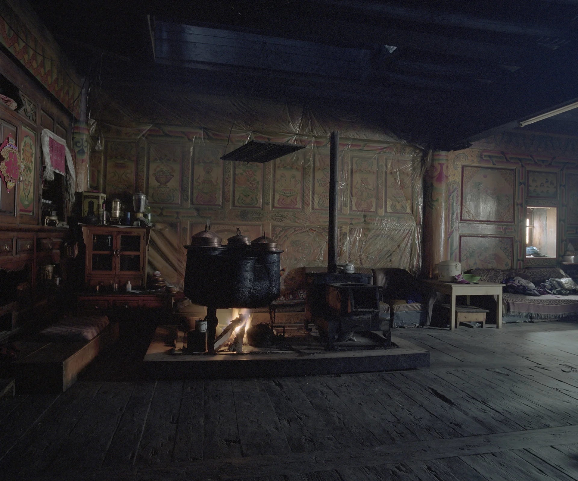 2010, Gezan - Life centers around the stove. Source of warmth and light in de evening. Food for people and catle is cooked here. The plastic at the walls is there to protect the paintings.