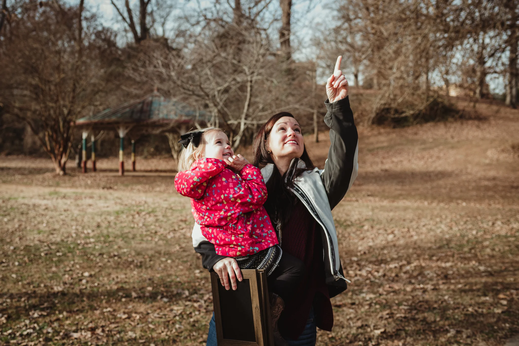 The three year old girl and her Mommy point to the sky during their family session in Raleigh, North Carolina.