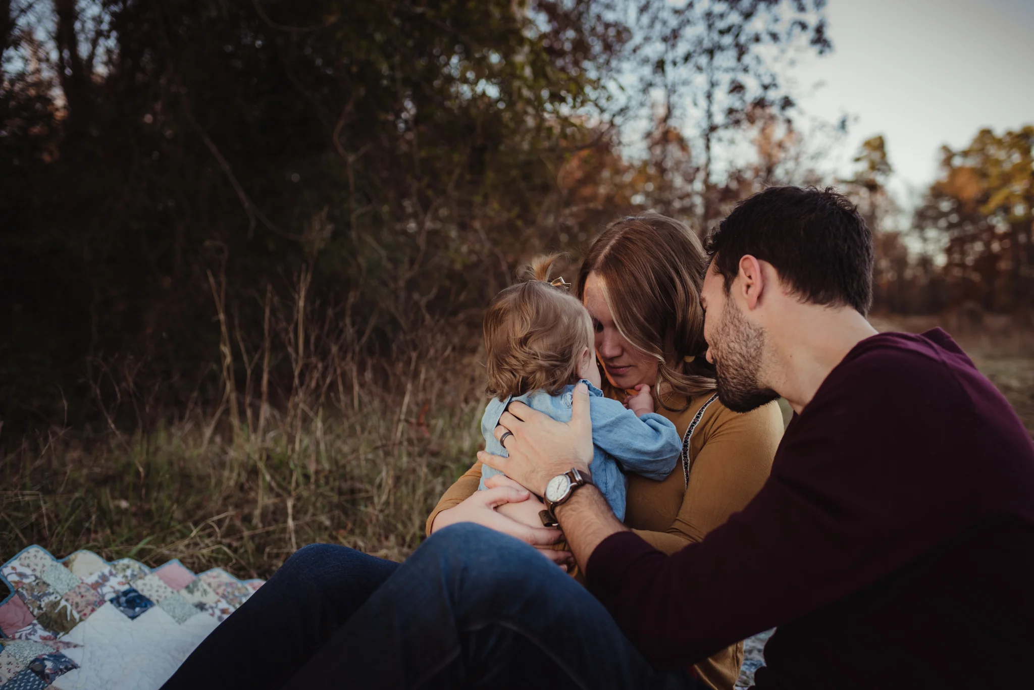 The family takes a moment to console their young daughter at sunset during their family photo session with Rose Trail Images at Horseshoe Nature Park in Wake Forest, NC.