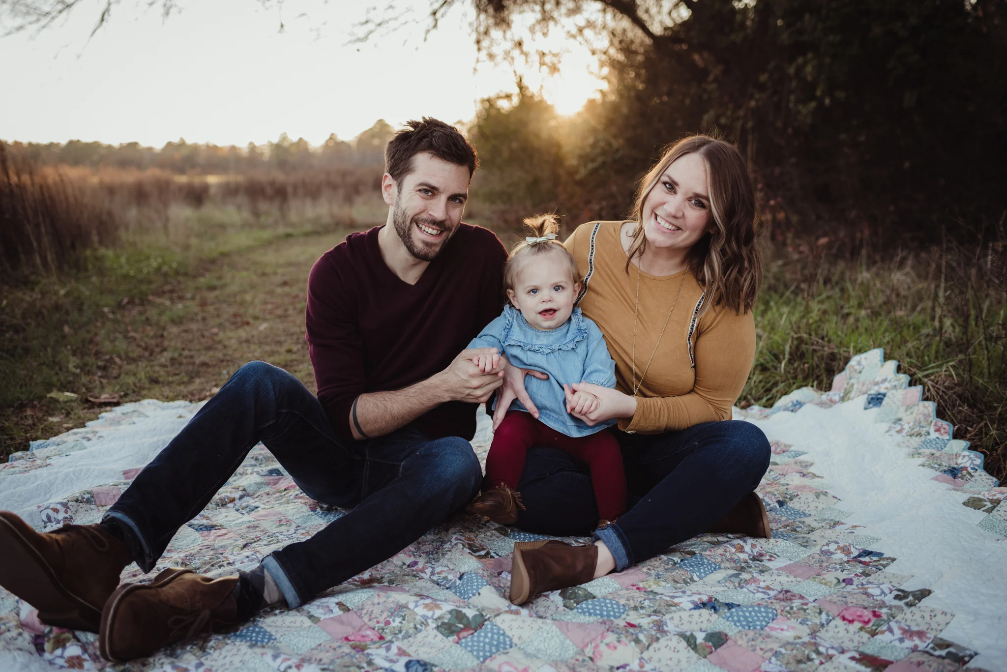 This young family sits with their young daughter on an old quilt at sunset during their family photo session with Rose Trail Images at Horseshoe Nature Park in Wake Forest, NC.