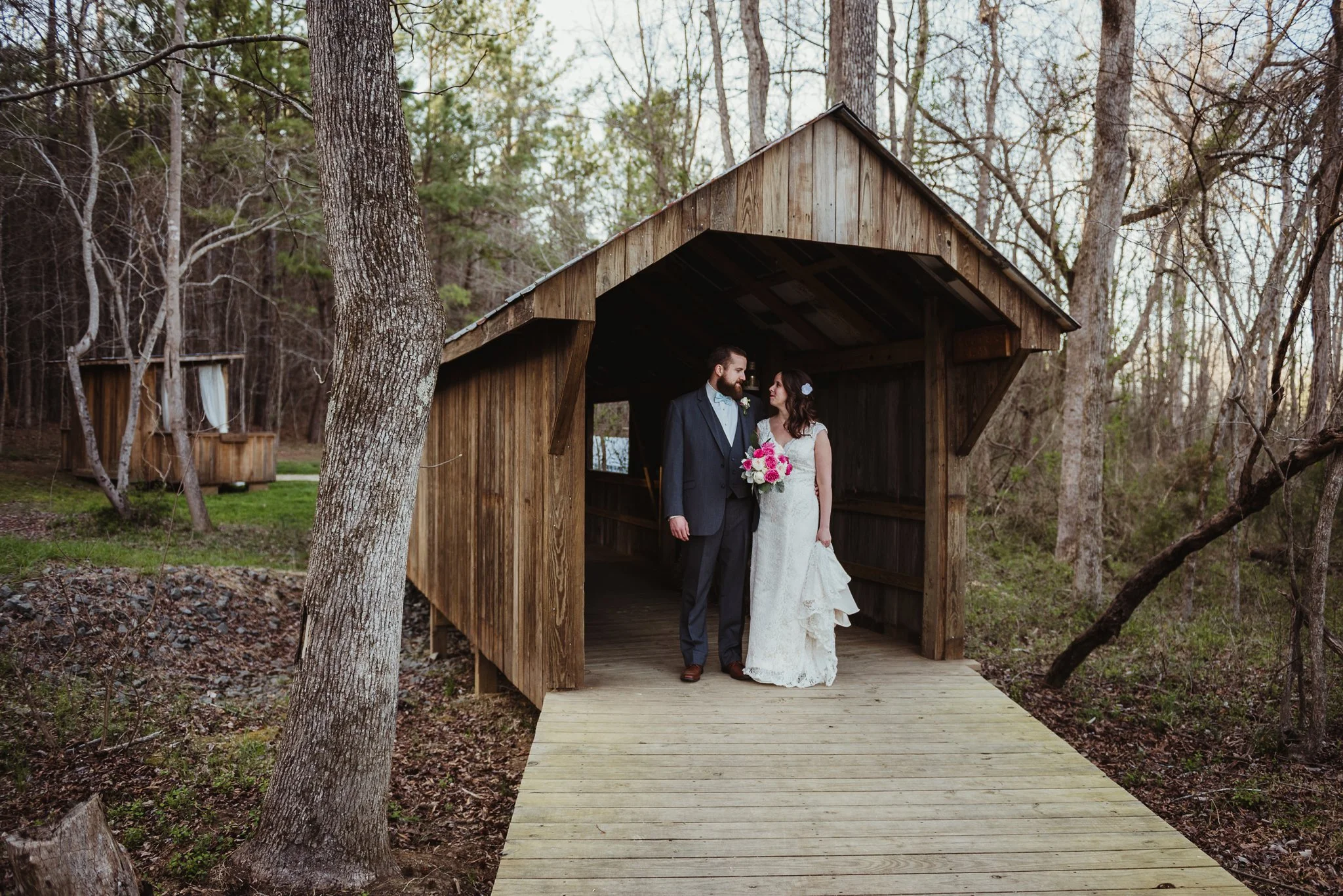 The bride and groom take pictures at the covered bridge after the wedding ceremony with Rose Trail Images at Carlee Farms in Oxford, NC.