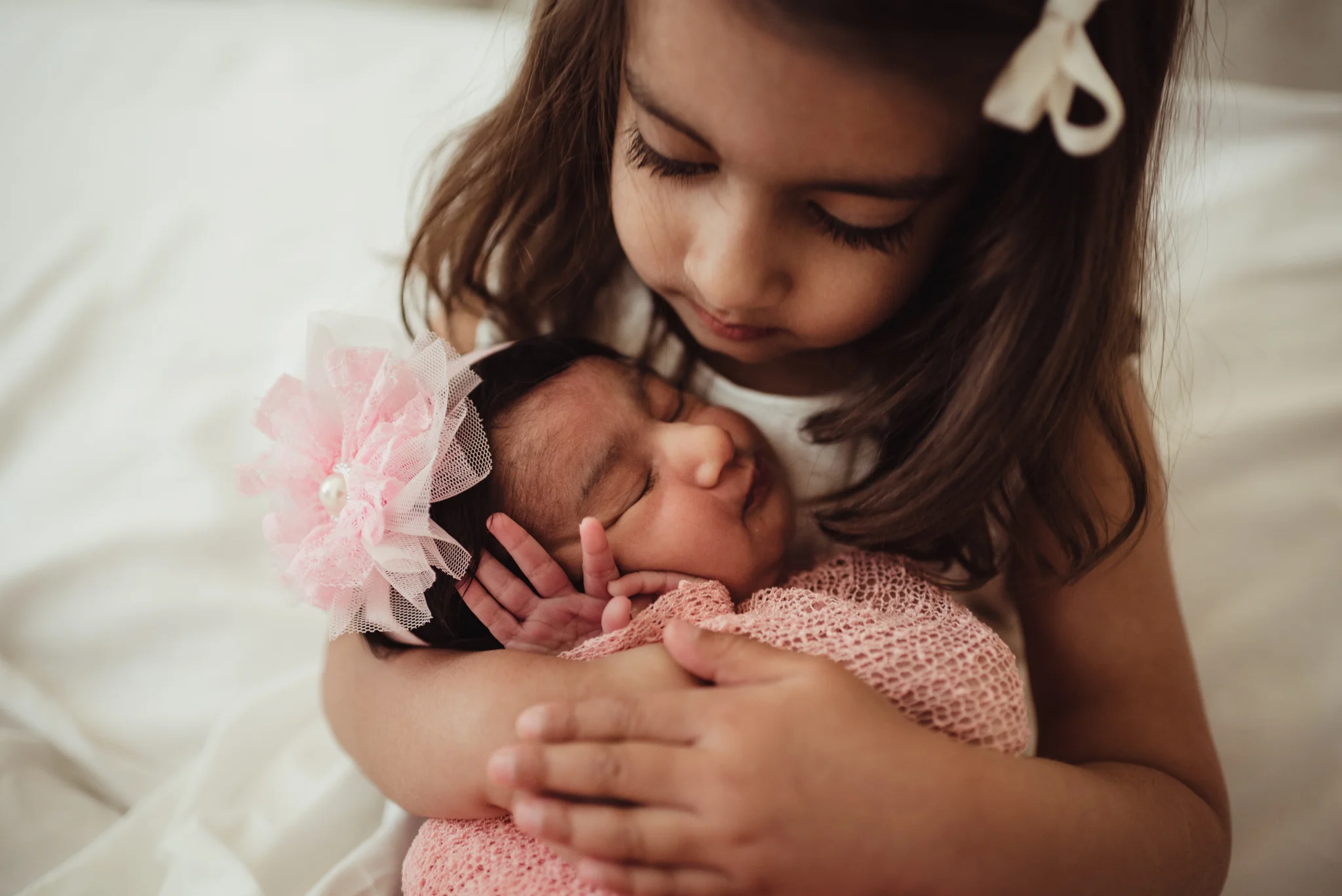 Older sister hugs her new baby sister on their parents' bed during their lifestyle newborn session with Rose Trail Images in Raleigh, North Carolina. 