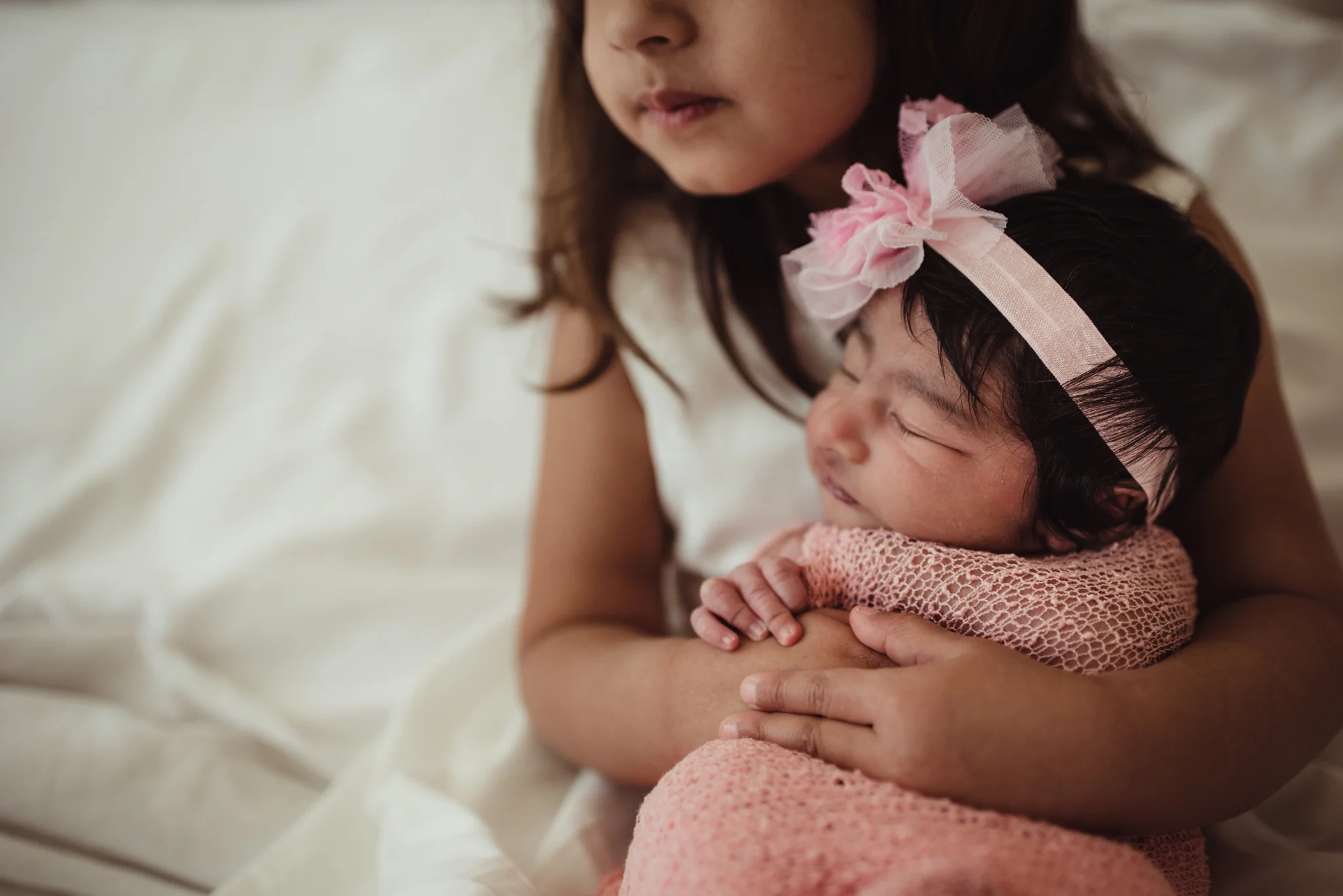 Older sister holds her new baby sister on their parents' bed during their lifestyle newborn session with Rose Trail Images in Raleigh, North Carolina. 