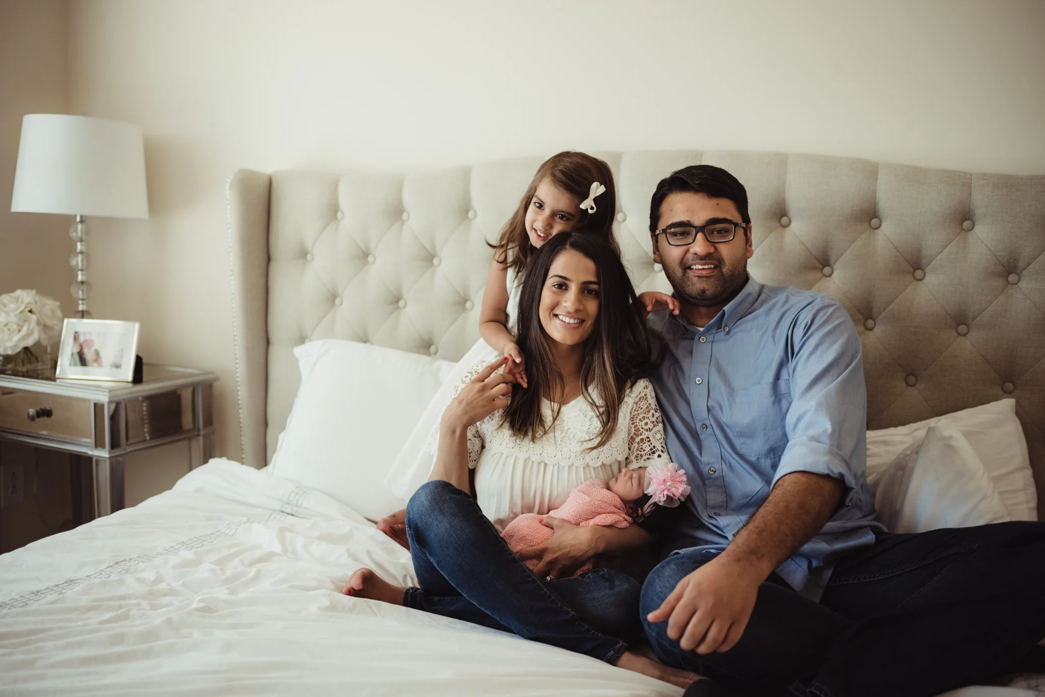 The new family of four pose on the bed during their lifestyle newborn session with Rose Trail Images in Raleigh, North Carolina. 
