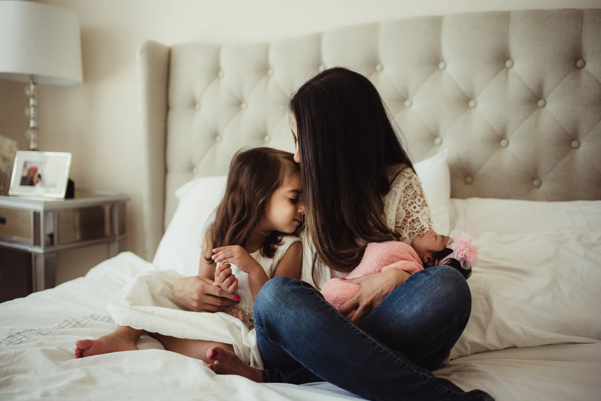 Mom sits with her two daughters on the bed during their lifestyle newborn session with Rose Trail Images in Raleigh, North Carolina. 
