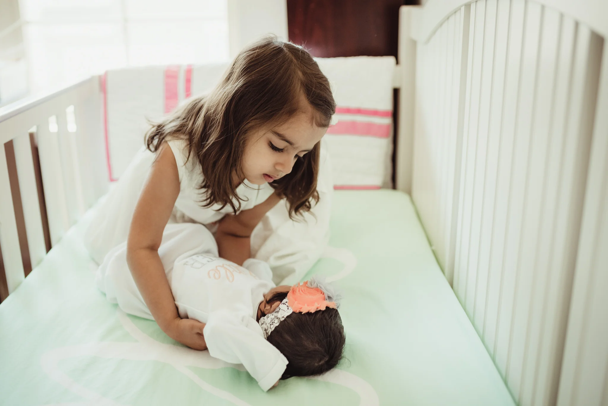 The newborn baby girl lay in her crib with her big sister during her lifestyle newborn session with Rose Trail Images in Raleigh, North Carolina. 