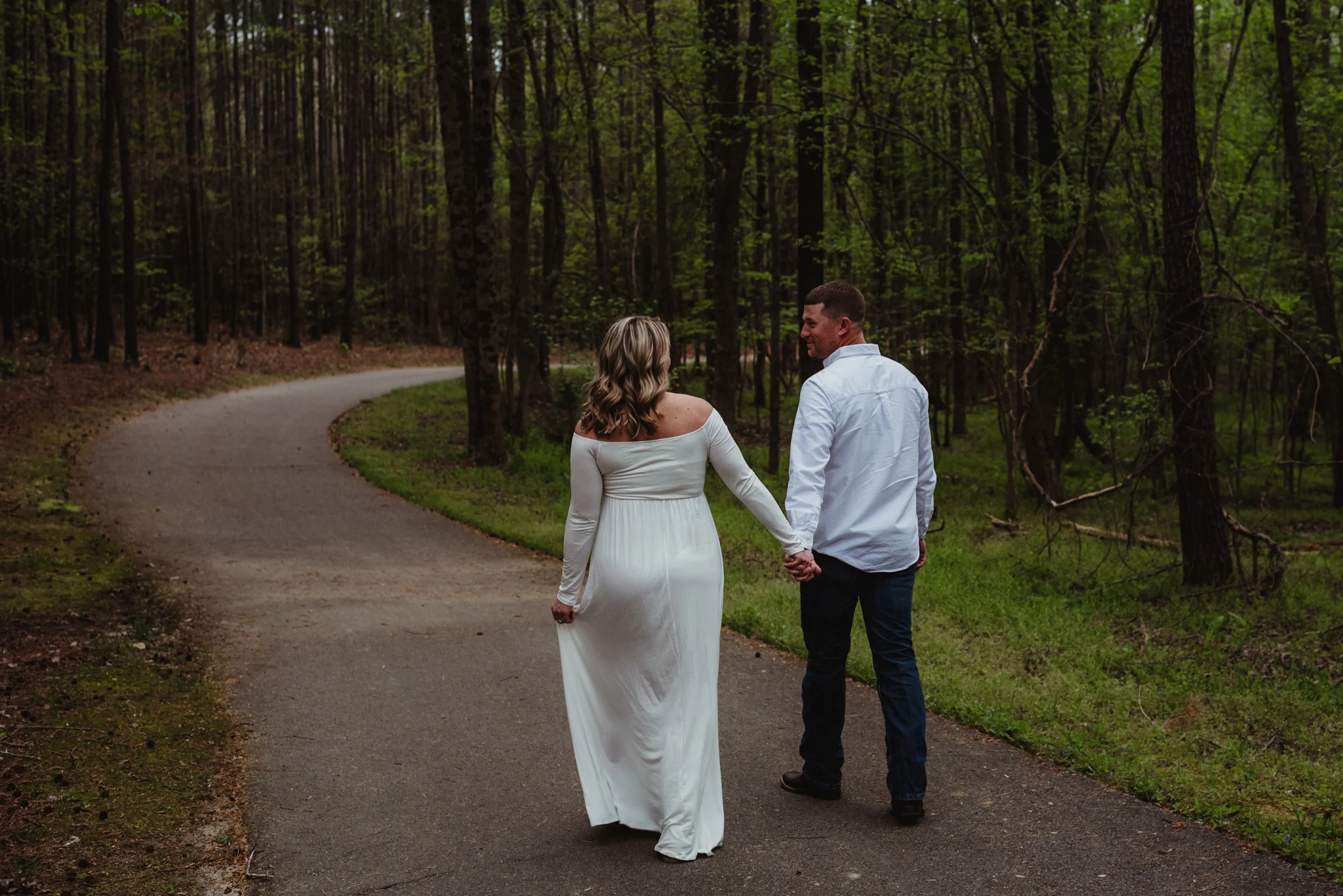 The soon to be parents walk down the trail during their maternity shoot with Rose Trail Images at Mill Bridge Nature Park in Rolesville, NC.