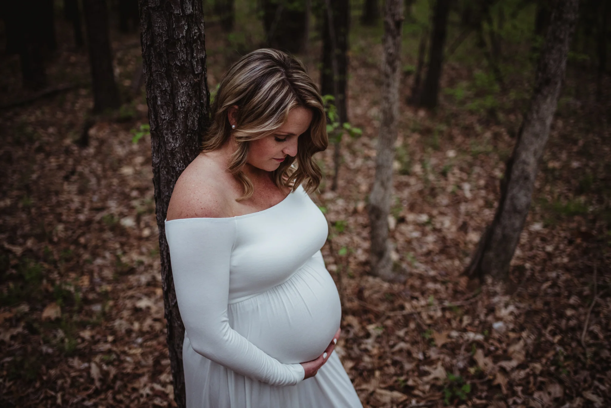 The pregnant Mama looks at her belly during her maternity shoot with Rose Trail Images at Mill Bridge Nature Park in Rolesville, NC.