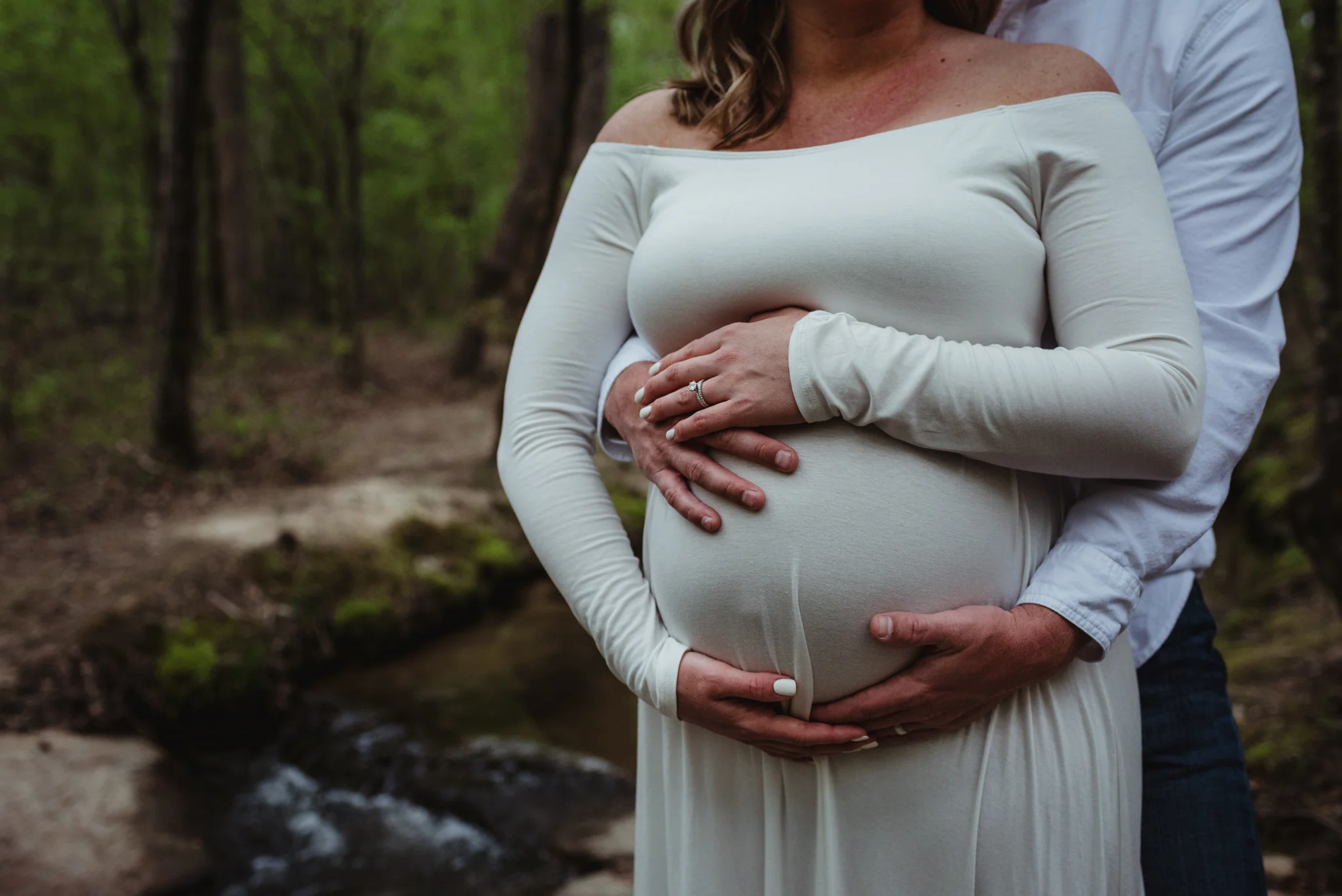 The soon to be parents wrap their hands around the belly during their maternity shoot with Rose Trail Images at Mill Bridge Nature Park in Rolesville, NC.