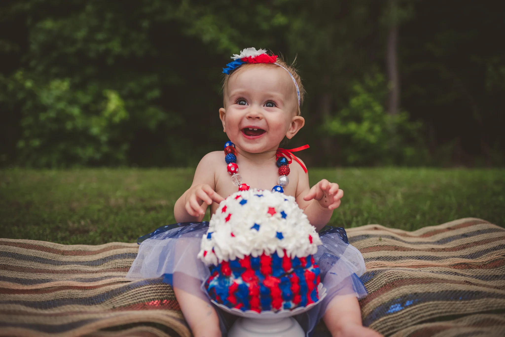 This little girl is getting ready to eat cake for her one year old fourth of July cake smash session with Rose Trail Images in Rolesville, North Carolina.