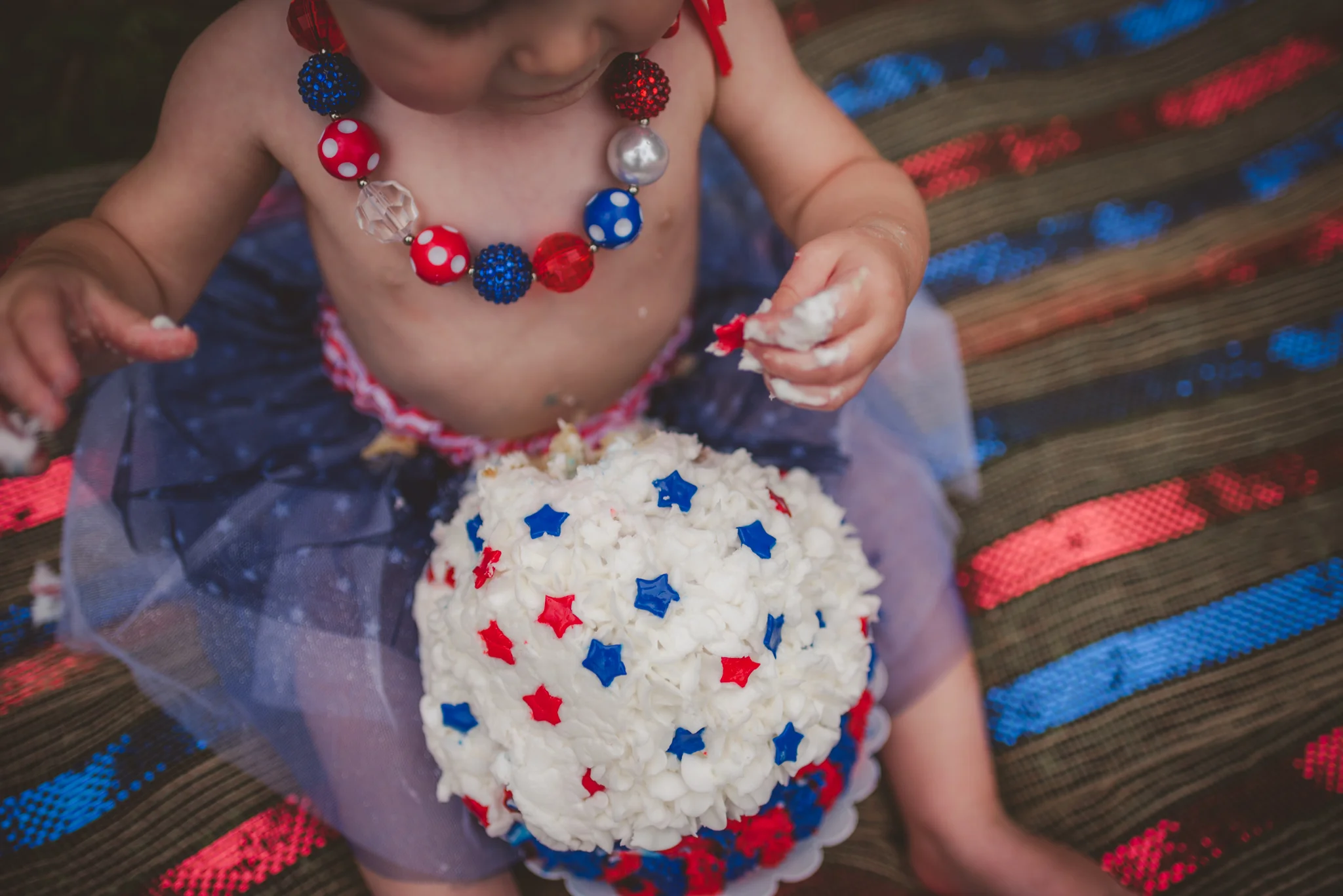 This little girl is eating her red, white and blue cake for her one year old fourth of July cake smash session with Rose Trail Images in Rolesville, North Carolina.
