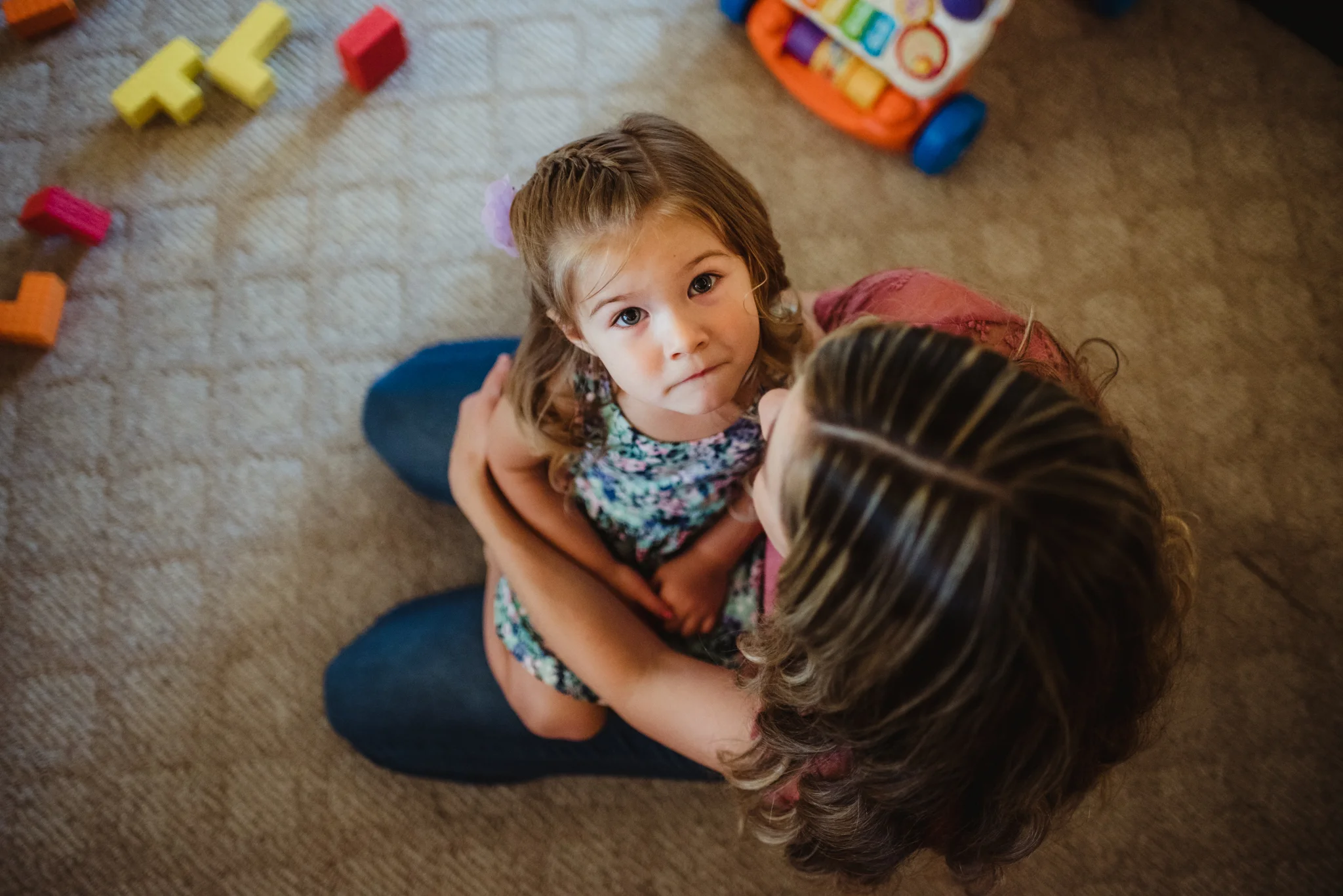 The little girl looks up from her Mom's lap during their lifestyle session at home in Wake Forest with Rose Trail Images.