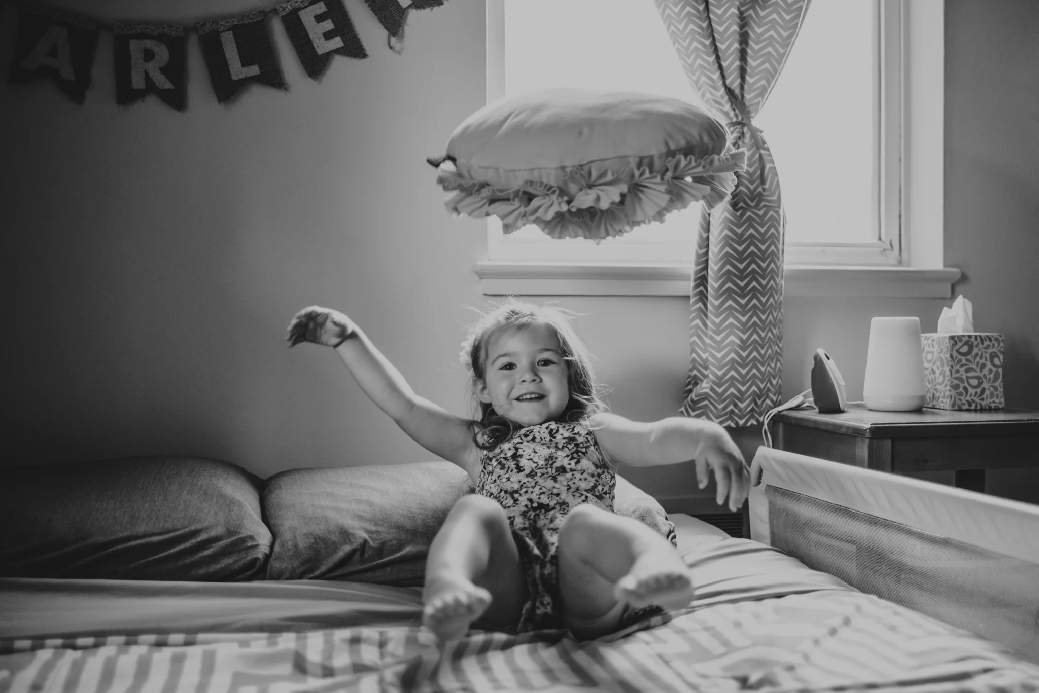 The little girl giggles on her bed during their lifestyle session at home in Wake Forest with Rose Trail Images.
