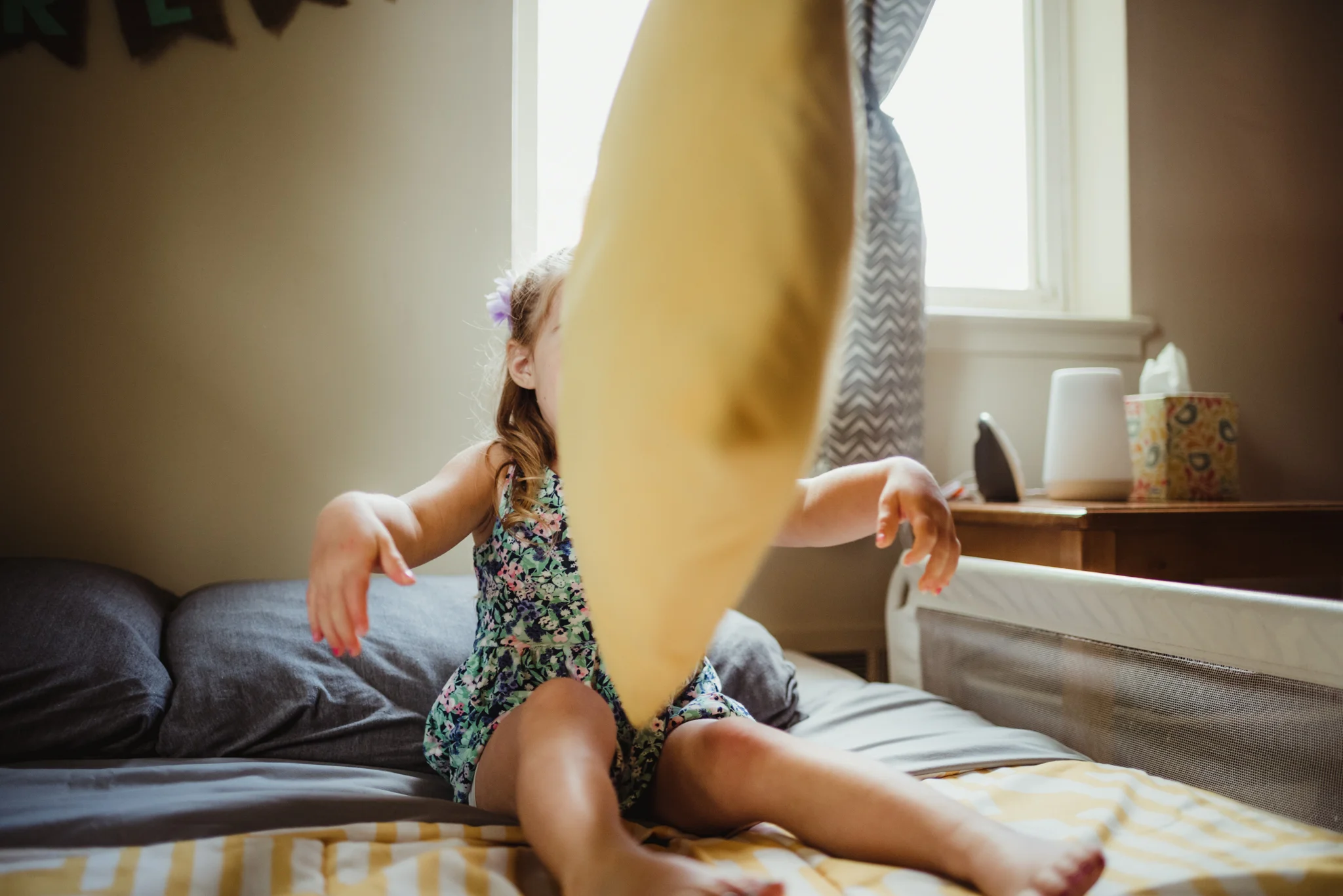 The little girl throws a pillow at the camera during her lifestyle session at home in Wake Forest with Rose Trail Images.