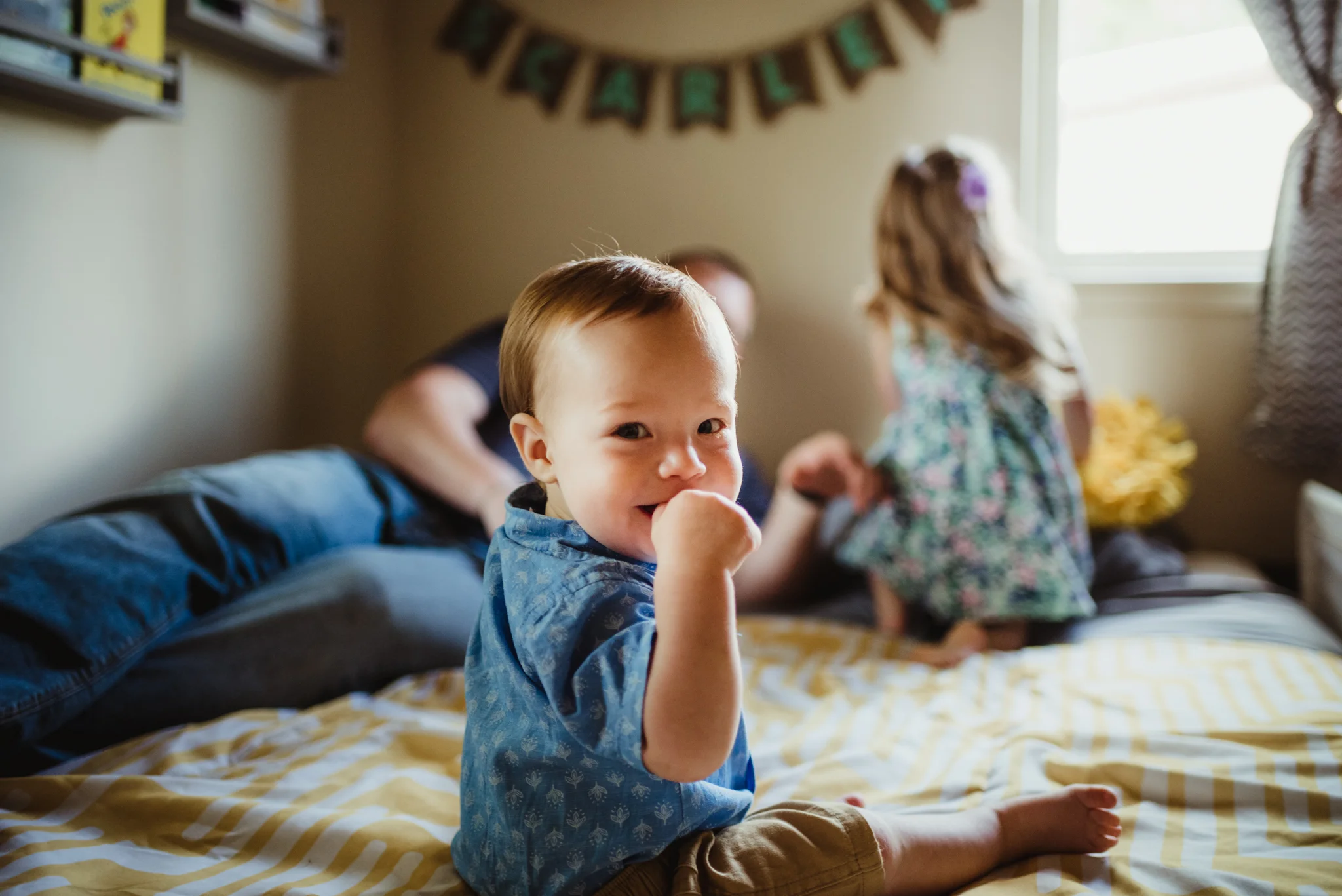 The baby smiles on the bed at the photographer during their lifestyle session at home in Wake Forest with Rose Trail Images.