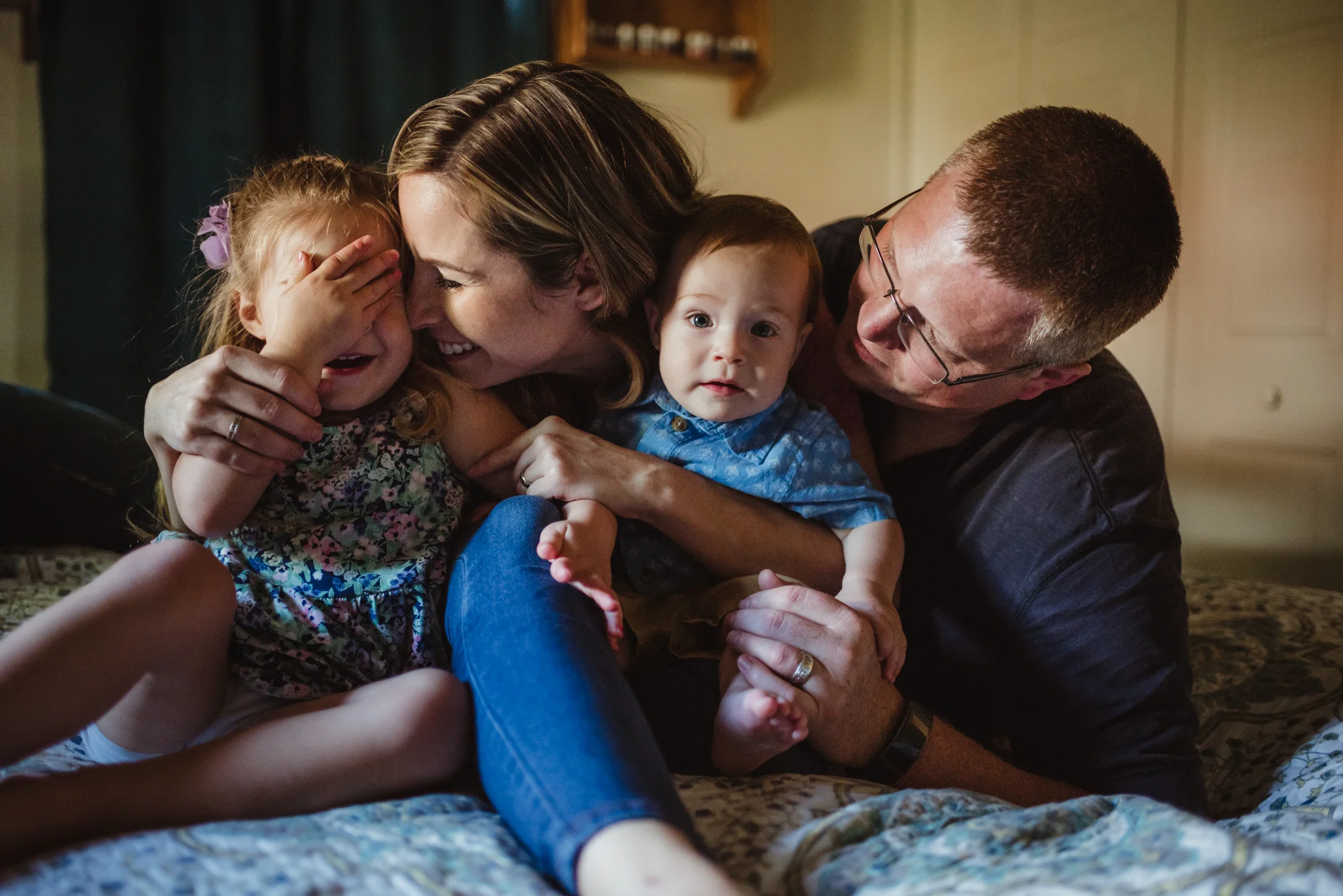 The family giggles together on the parents' bed during their lifestyle session at home in Wake Forest with Rose Trail Images.