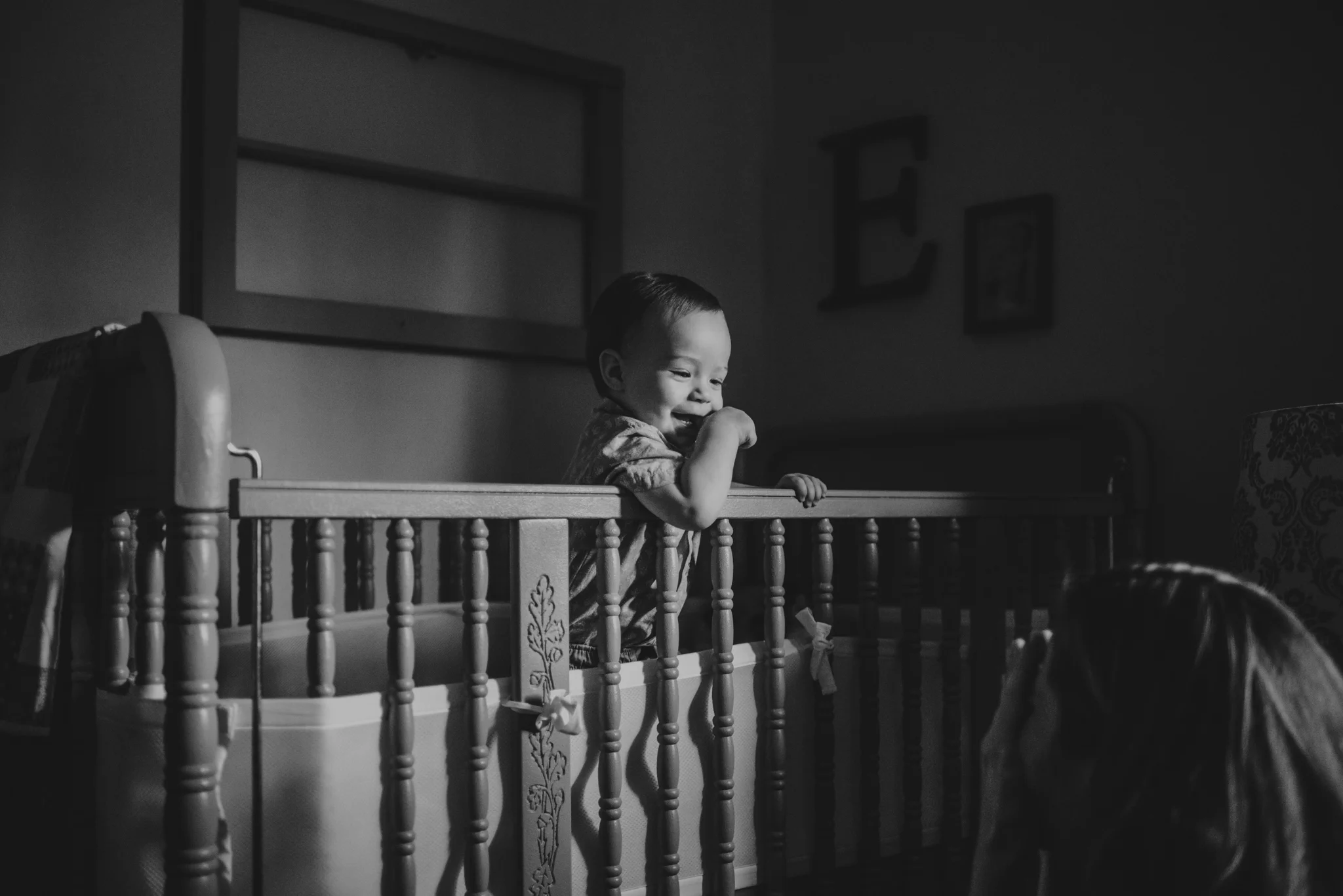 The baby giggles at his Mom while in his crib during their lifestyle session at home in Wake Forest with Rose Trail Images.