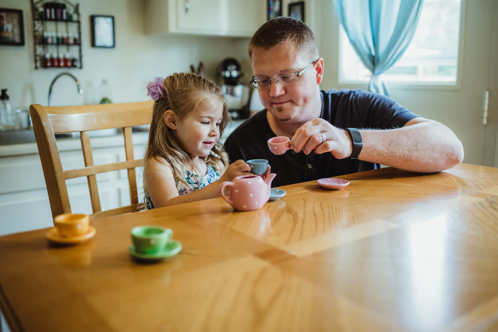 The little girl and Dad have tea time in the kitchen during their lifestyle session at home in Wake Forest with Rose Trail Images.