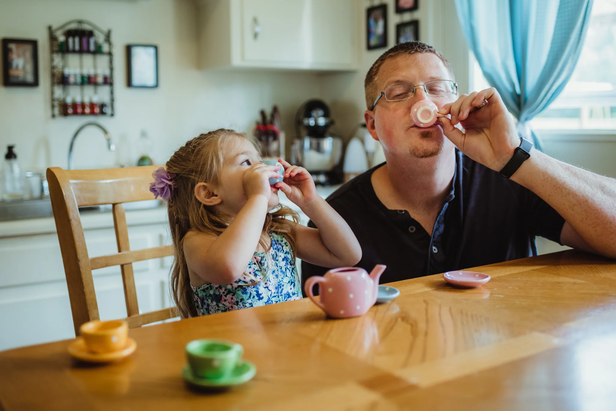The little girl and Dad have tea time in the kitchen during their lifestyle session at home in Wake Forest with Rose Trail Images.